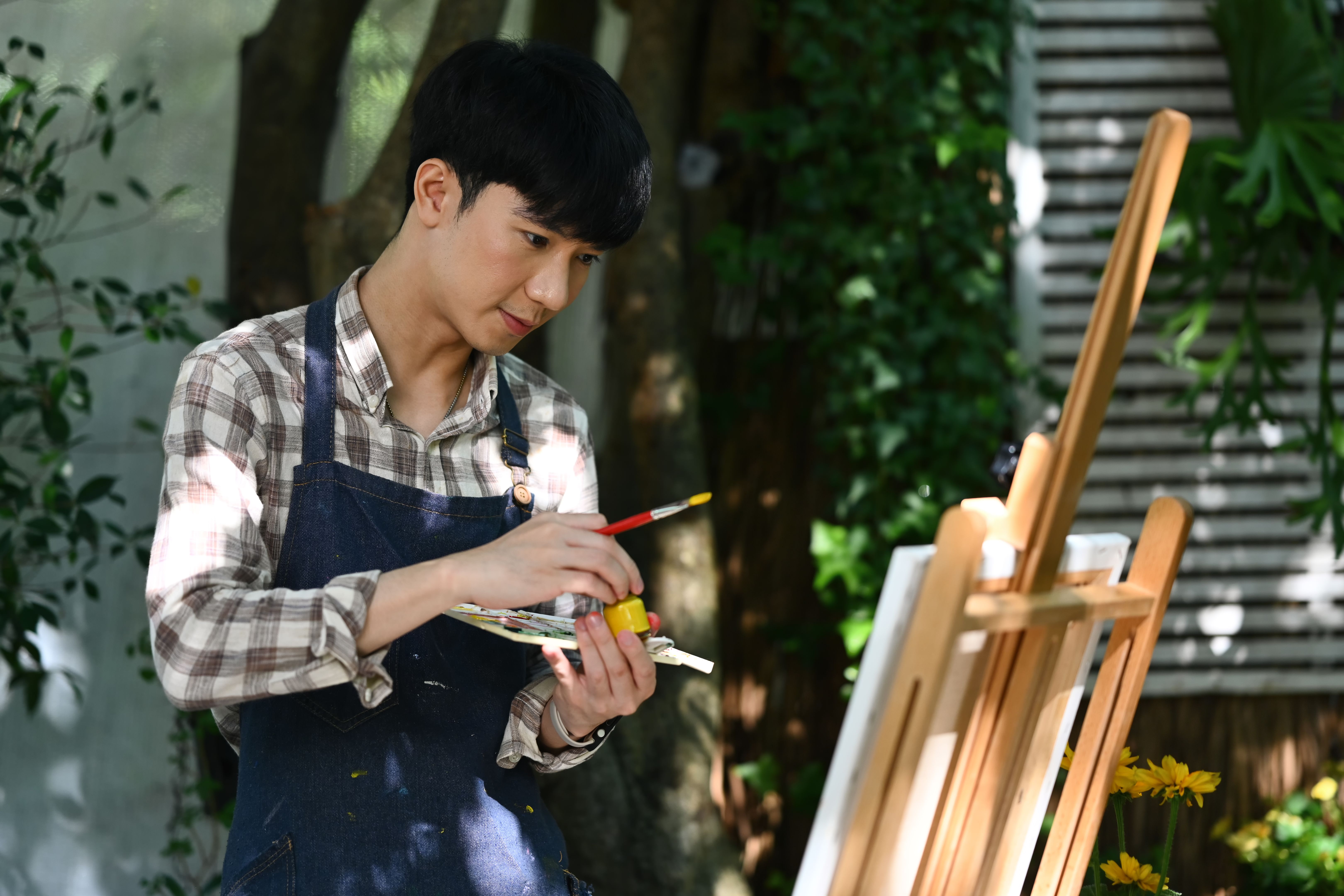 Handsome Asian man in apron painting with watercolor in garden on beautiful day.