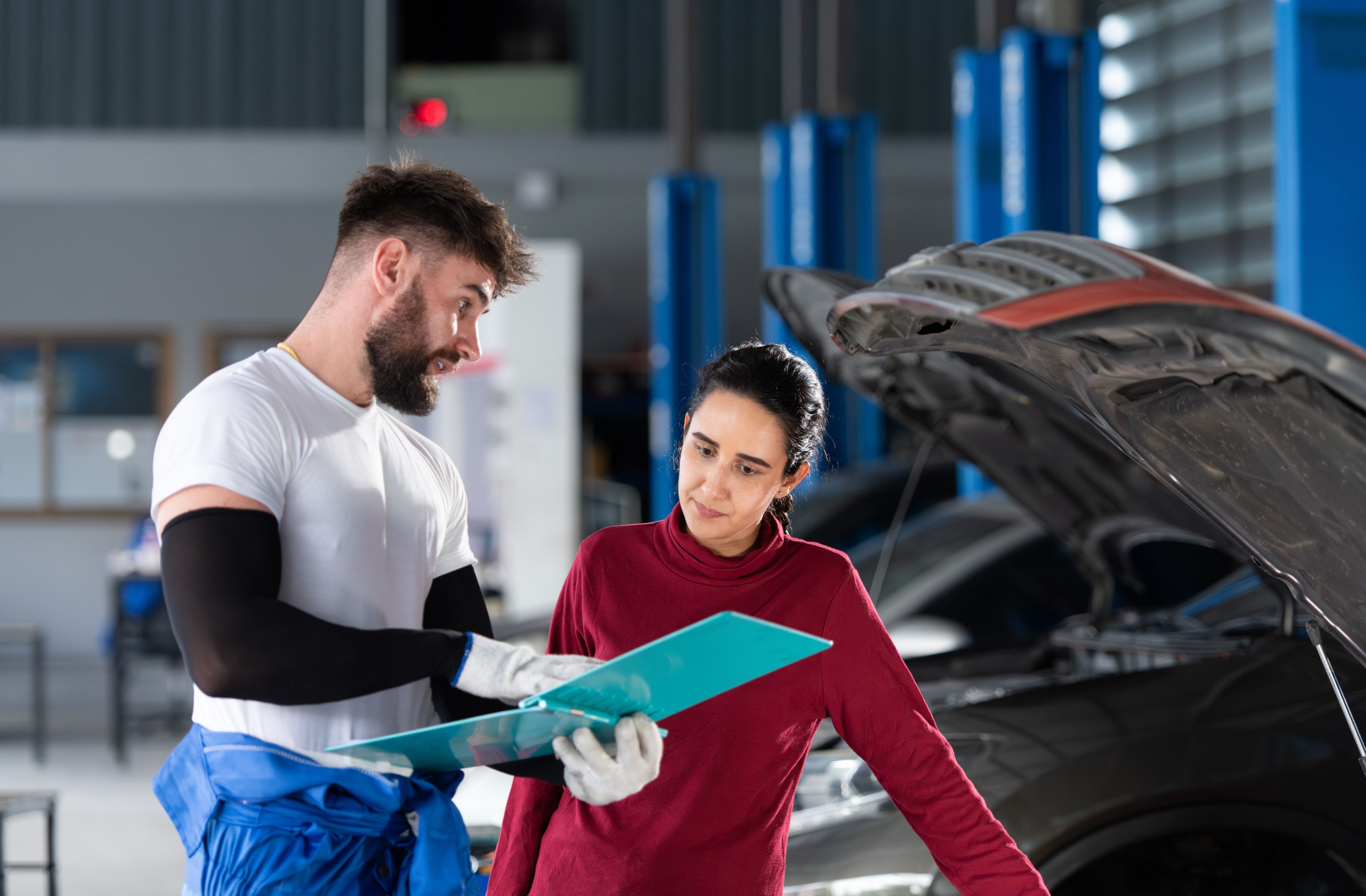 In an auto repair shop, A man professional auto mechanic briefs a female customer about the cost of car repairs and collects payment.