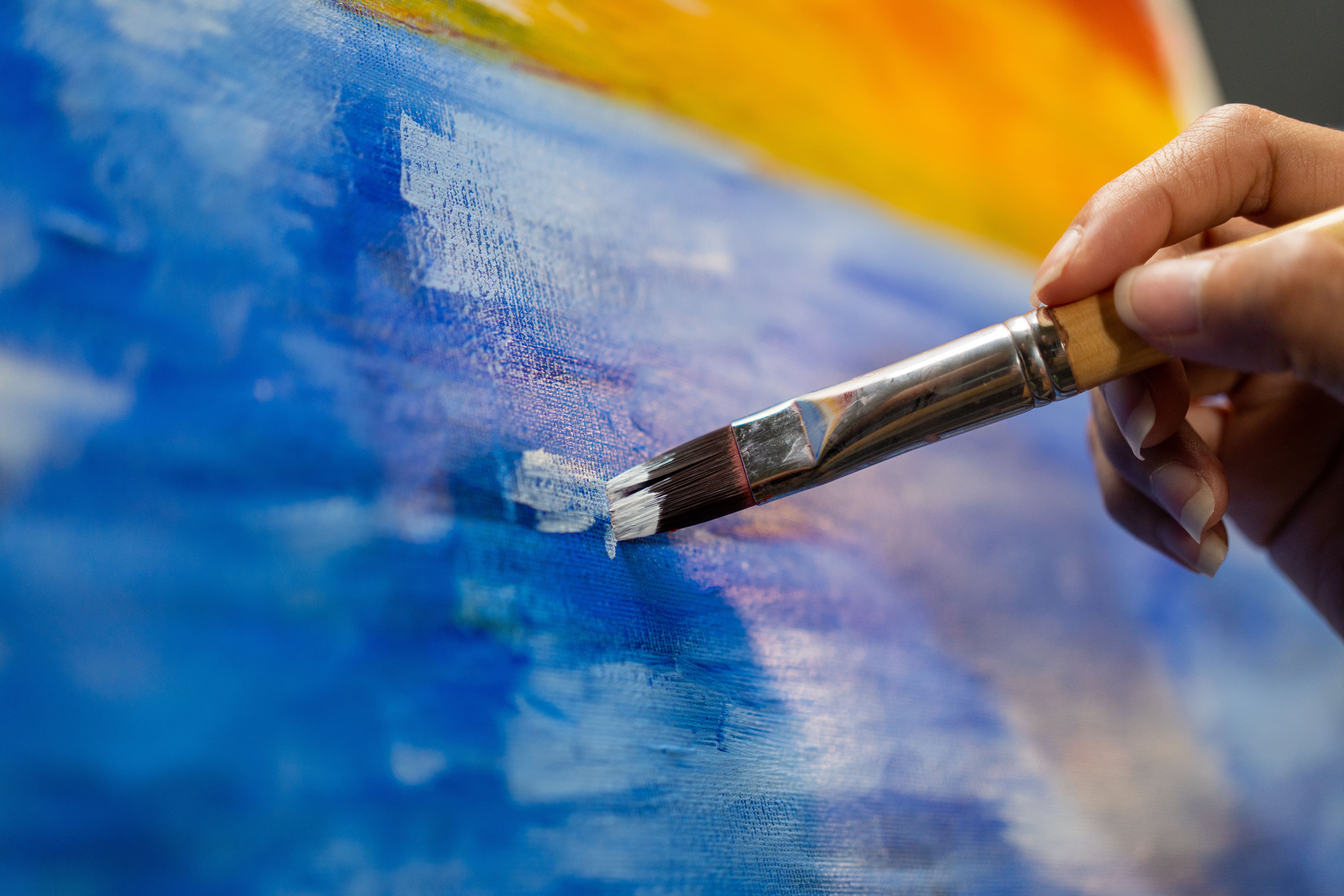 Close up woman hand artist in the darkroom warm light working on painting with brush and variant acrylic color. Female artist painter on canvas in creative studio as art concept