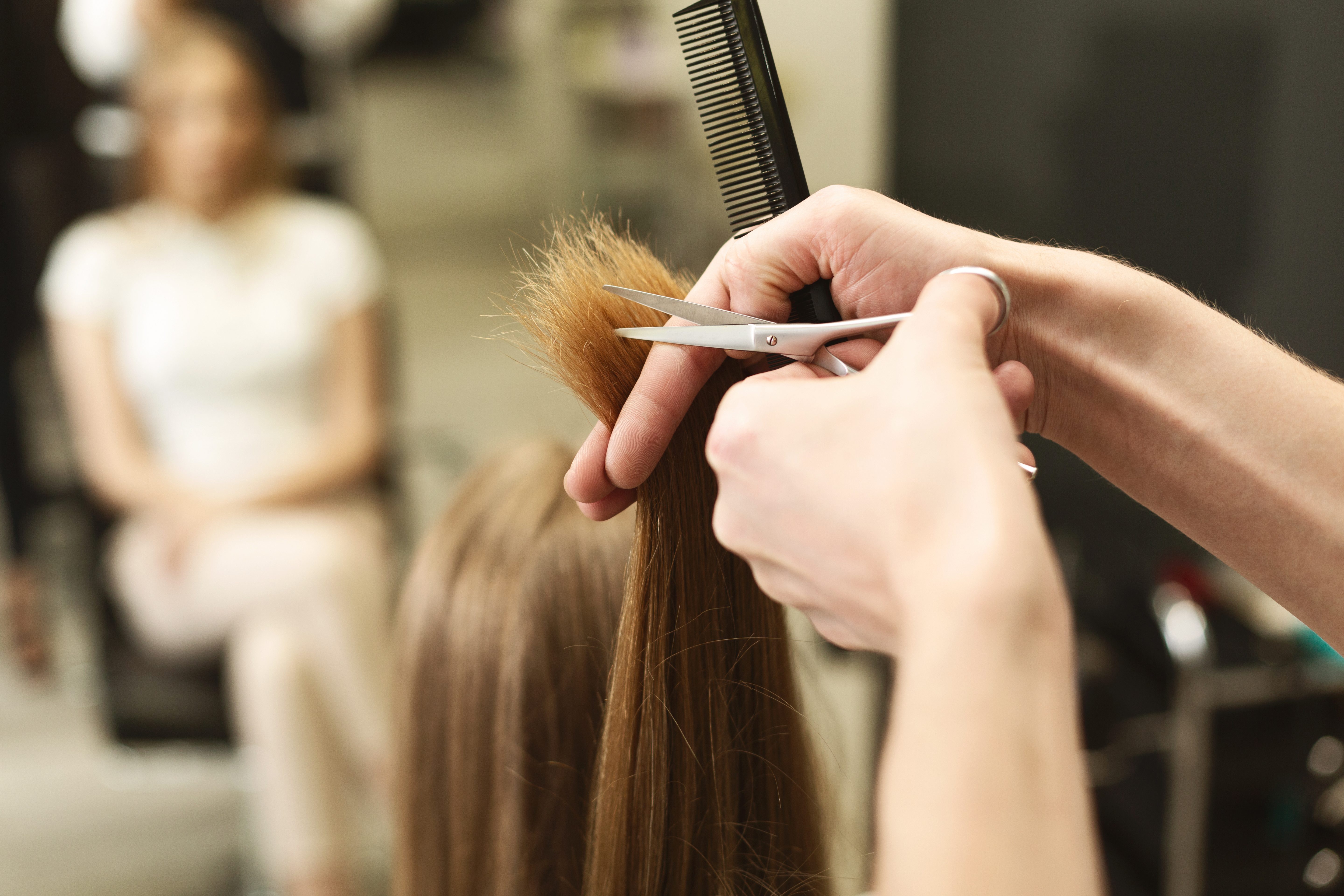 Closeup Of Hairdresser's Hands Trimming Split Ends On Female Hair In Salon