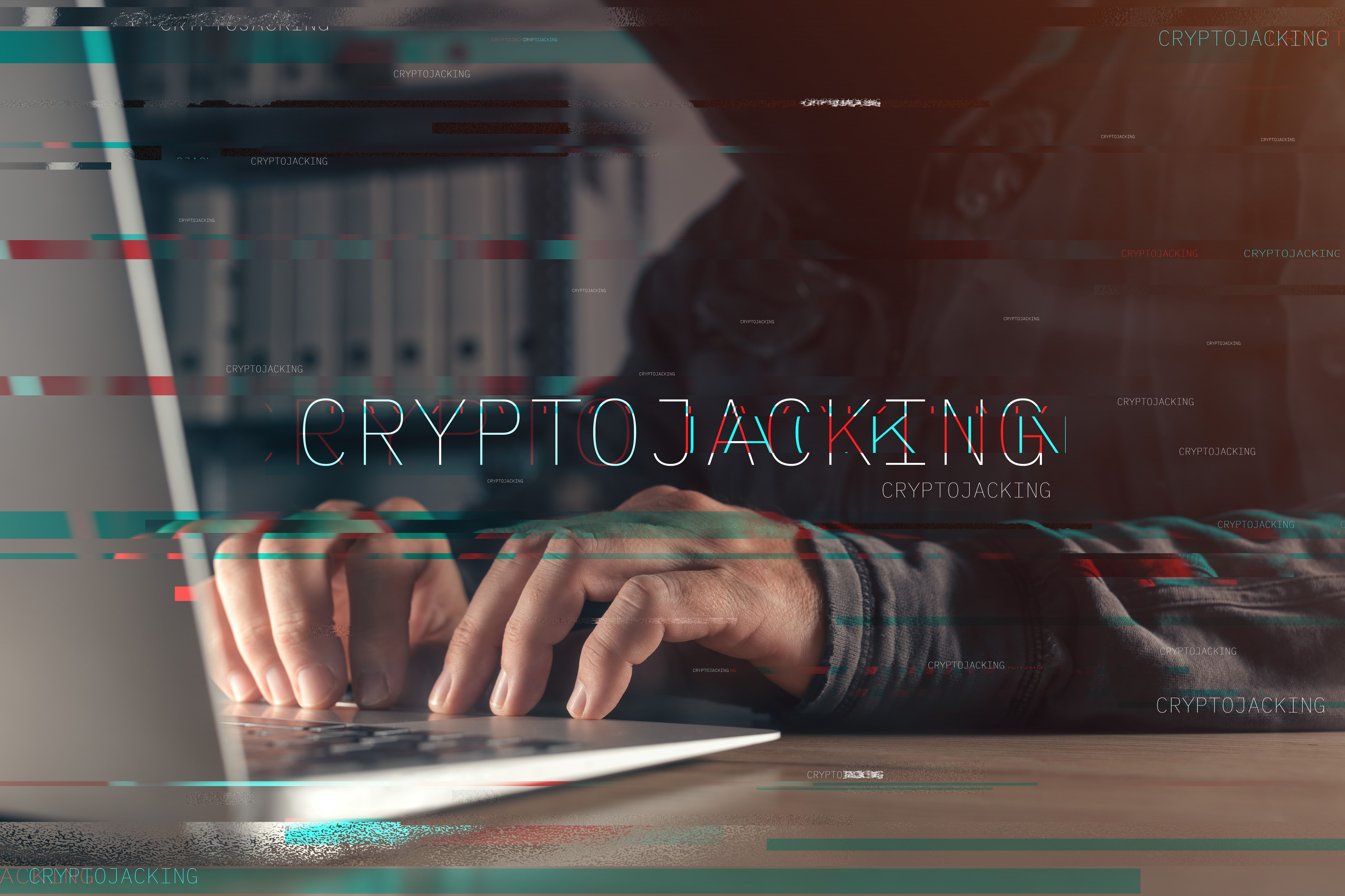 Cryptojacking concept with faceless hooded hacker working on laptop computer