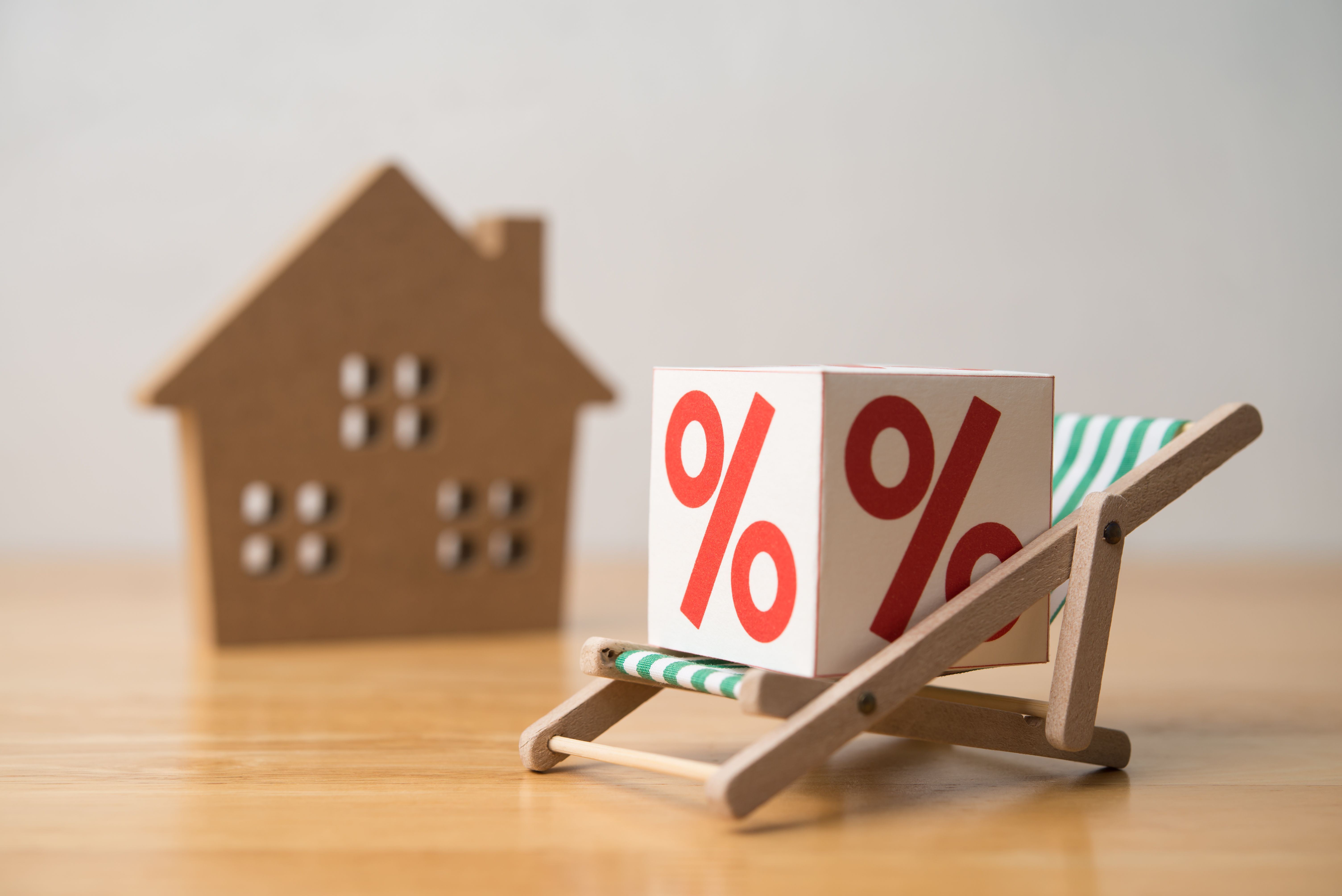 Percentage sign rests on beach chair with house model white wall background.
