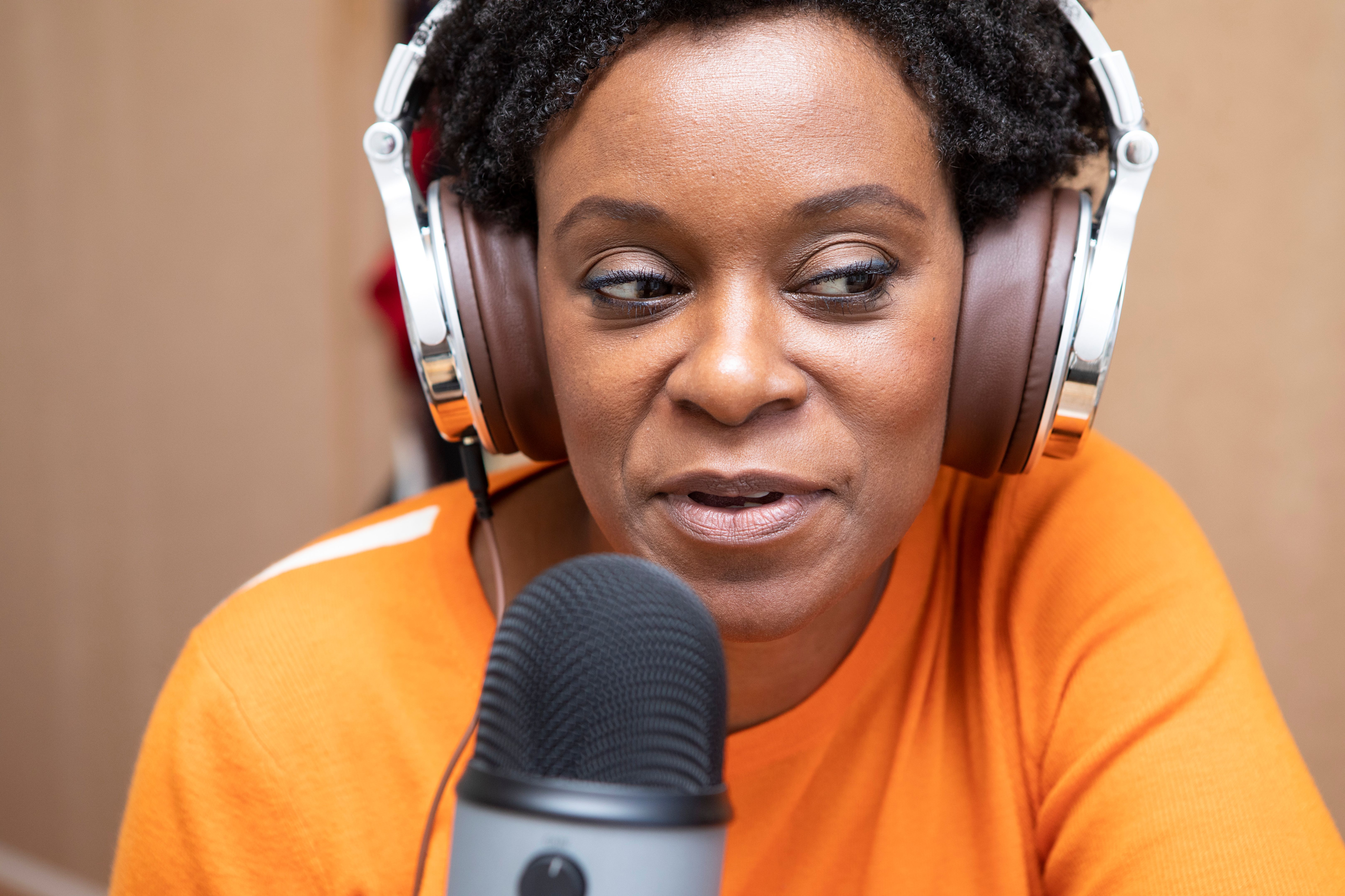 Headshot of a woman recording a podcast home in the bedroom - with headphones and a microphone