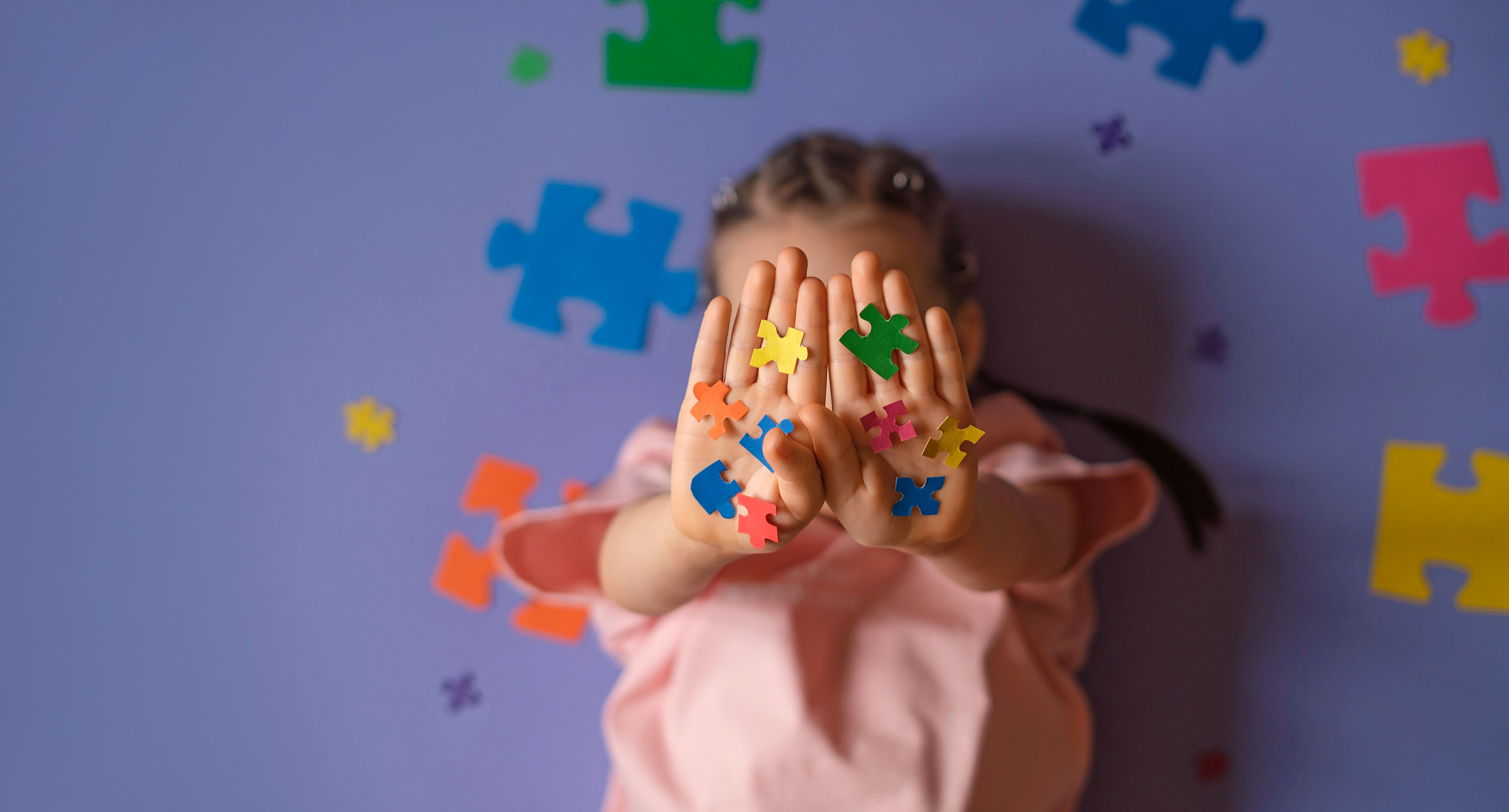 The child's palms are decorated with puzzle pieces in rainbow colors. A banner on the concept of awareness about autism. The child's palms are decorated with puzzle pieces in rainbow colors. A banner on the concept of awareness about autism.
