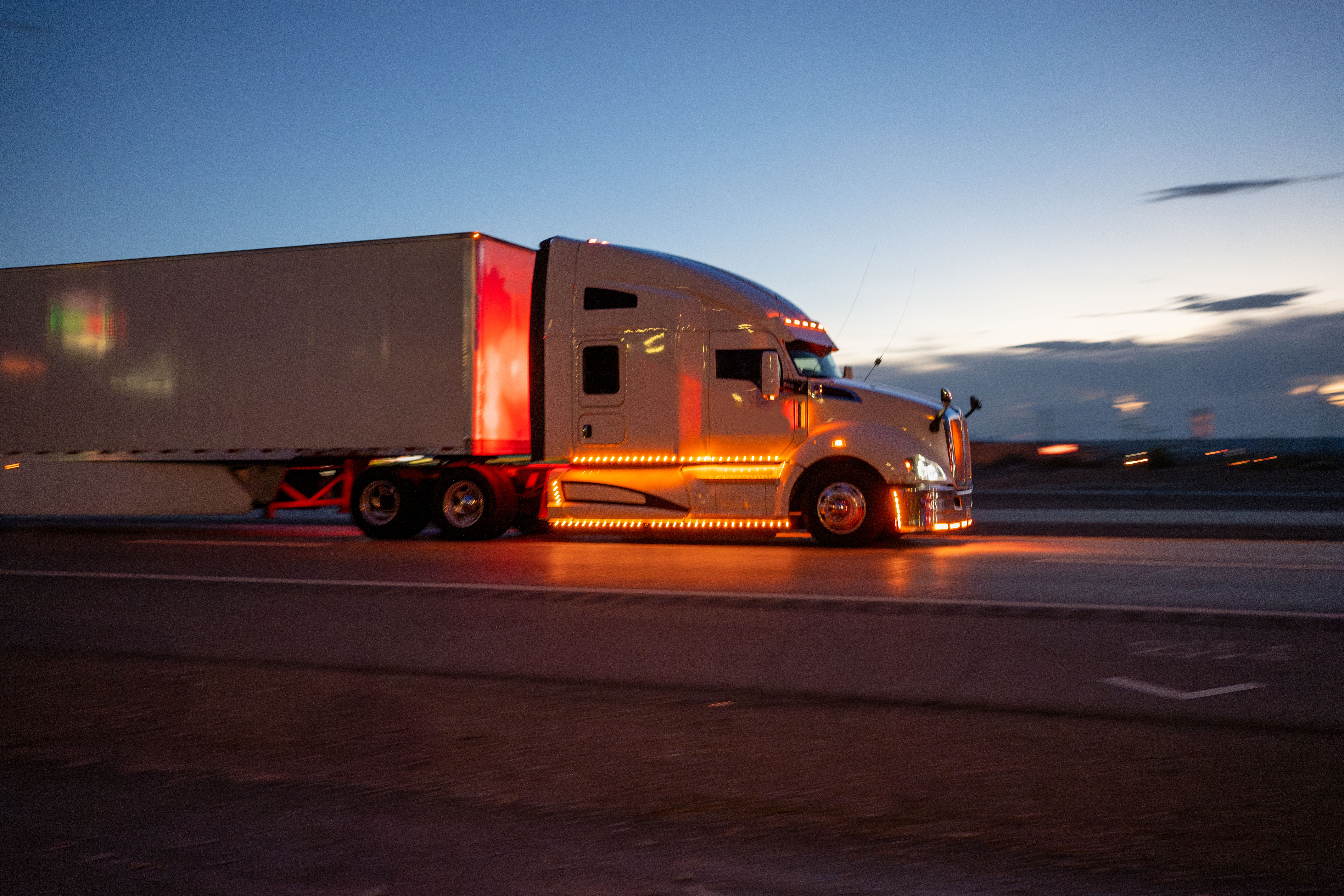 Cab of White Semi-Truck Speeding Down a Highway with a Stunning Cloudscape Sunset in the Background
