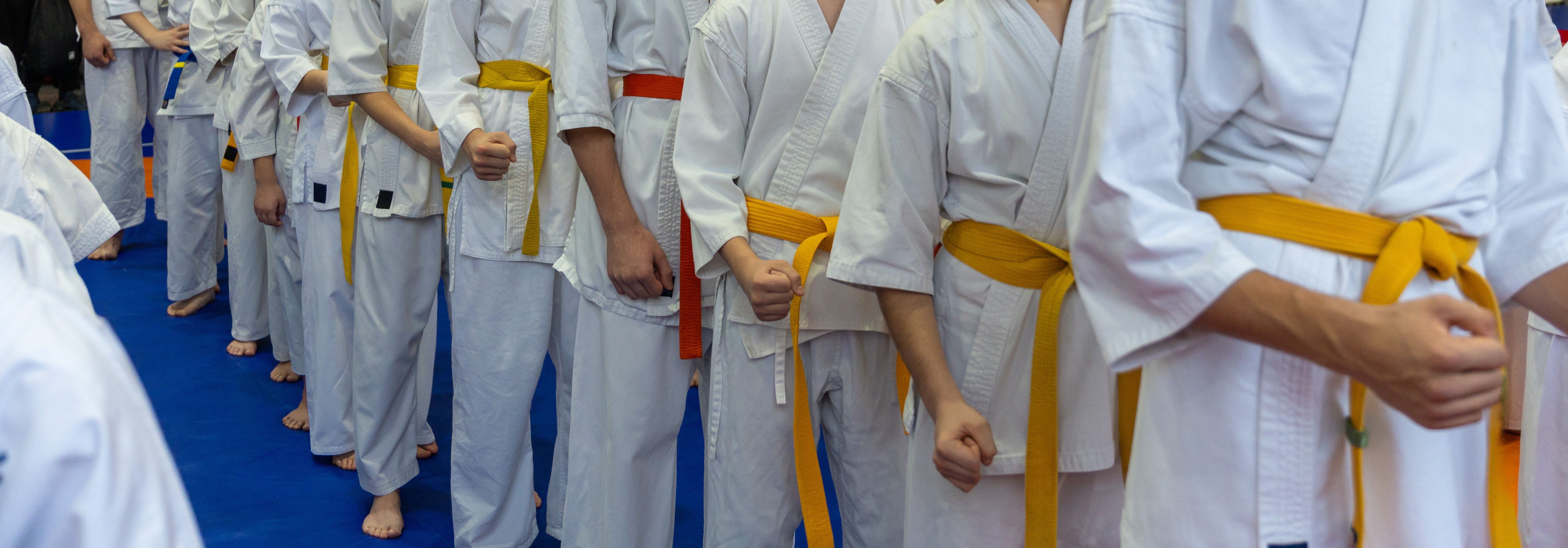 A close-up of a row of young athletes in white karate kimonos with clenched fists.
