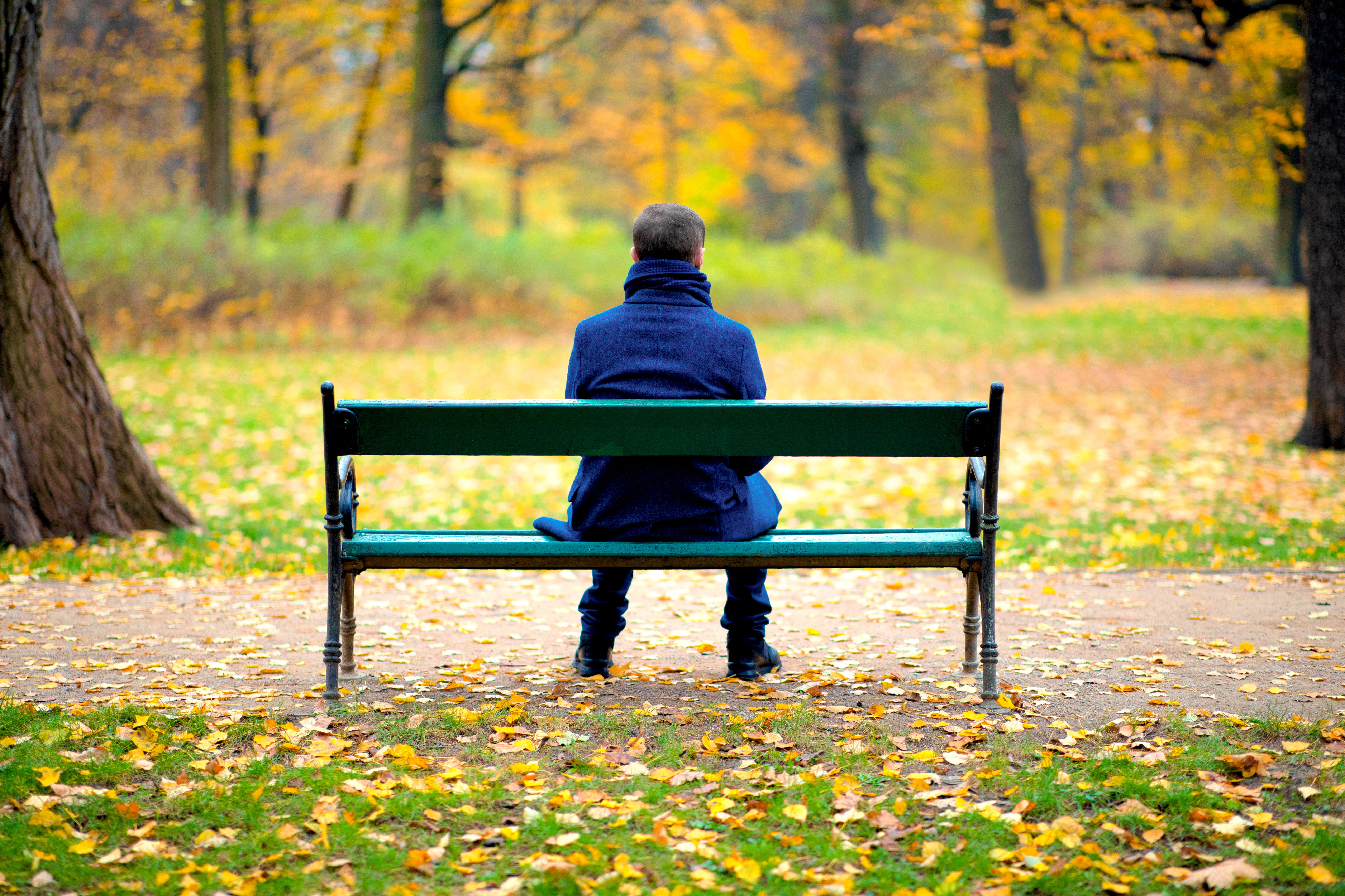 Lonely man sitting on a wooden bench outdoors in a park in autumn day Lonely man sitting on a wooden bench outdoors in a park in autumn day