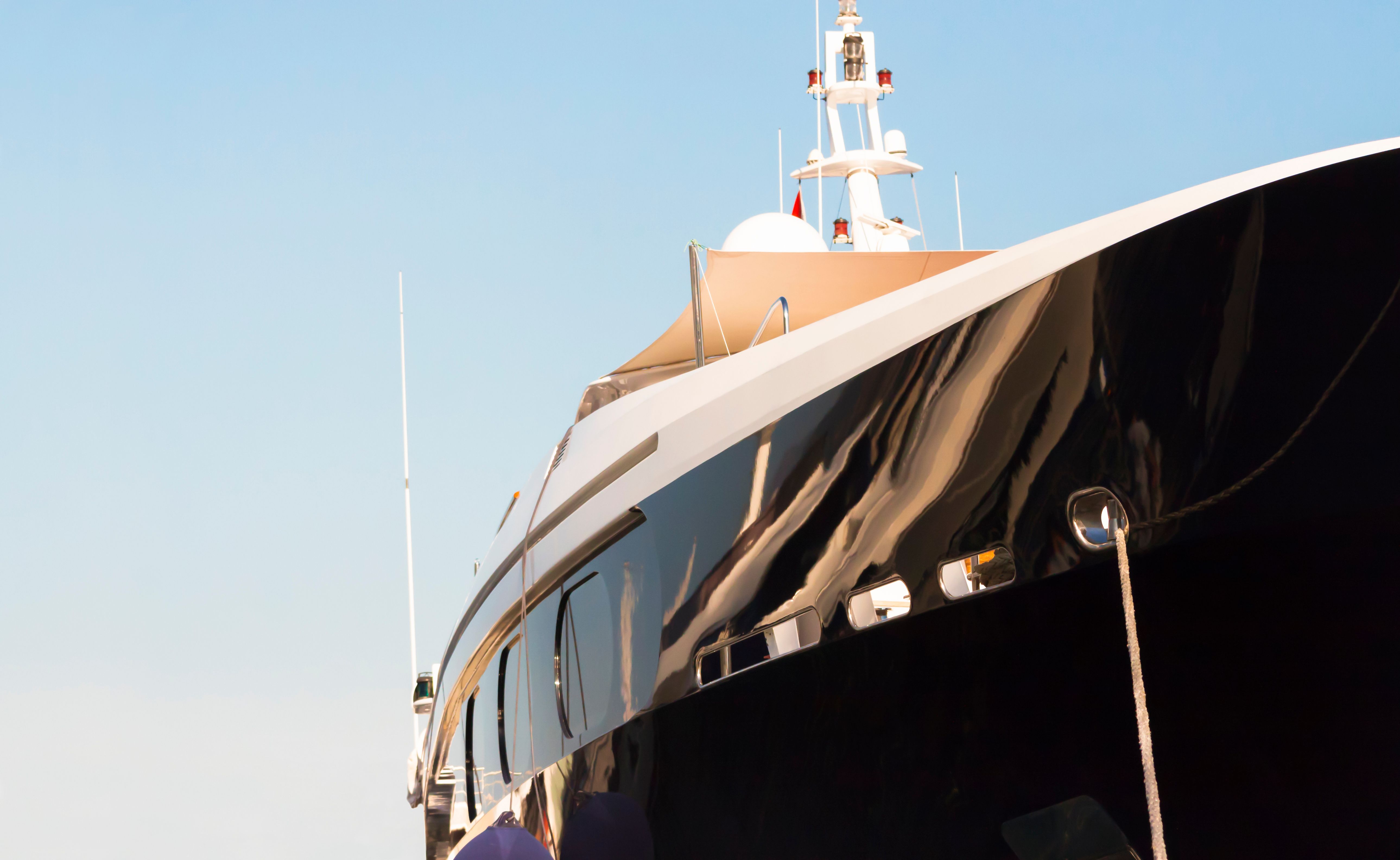 Side view of luxury black yacht in sunlight against sky