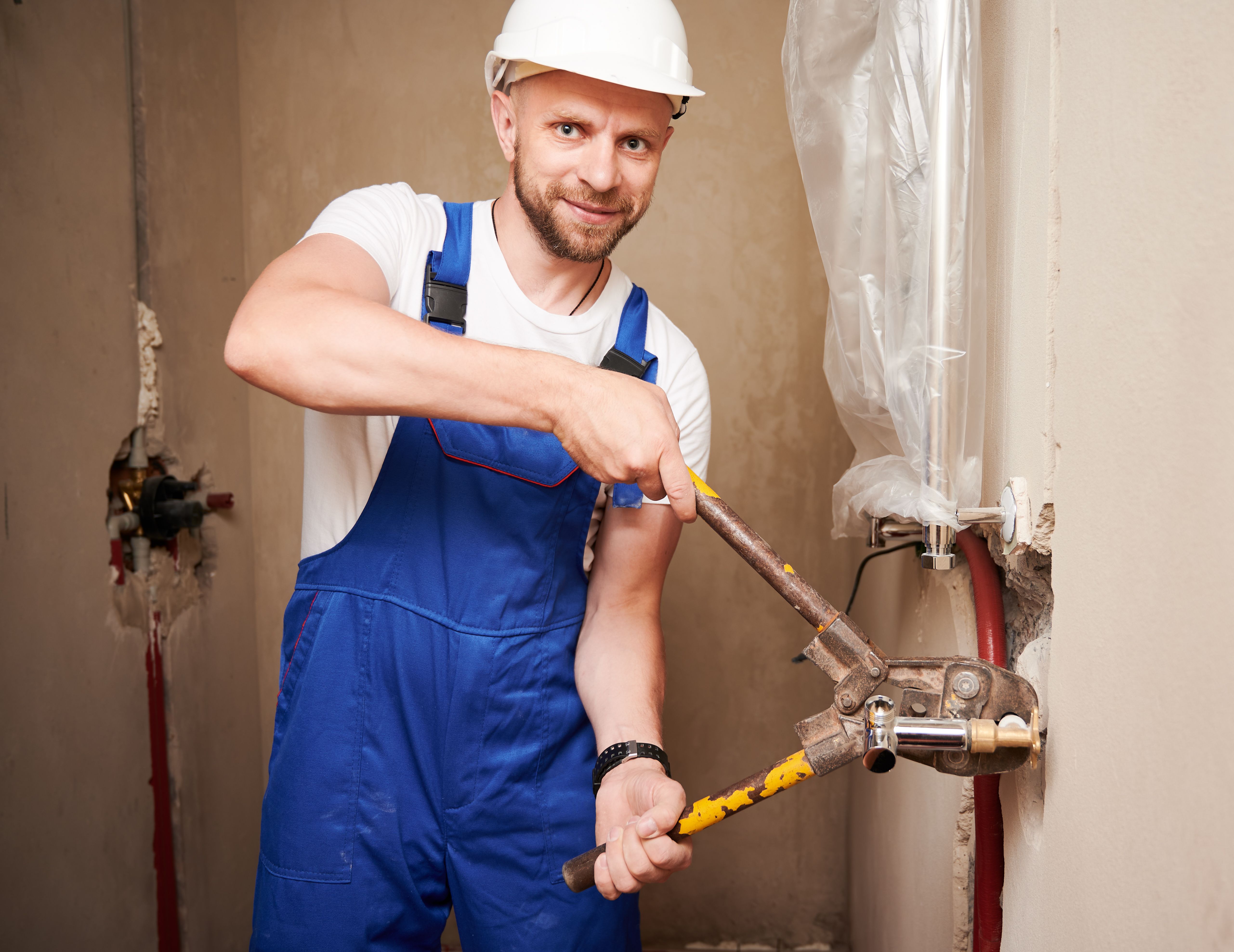 Man plumber using pipe pressing tool in apartment under renovation.