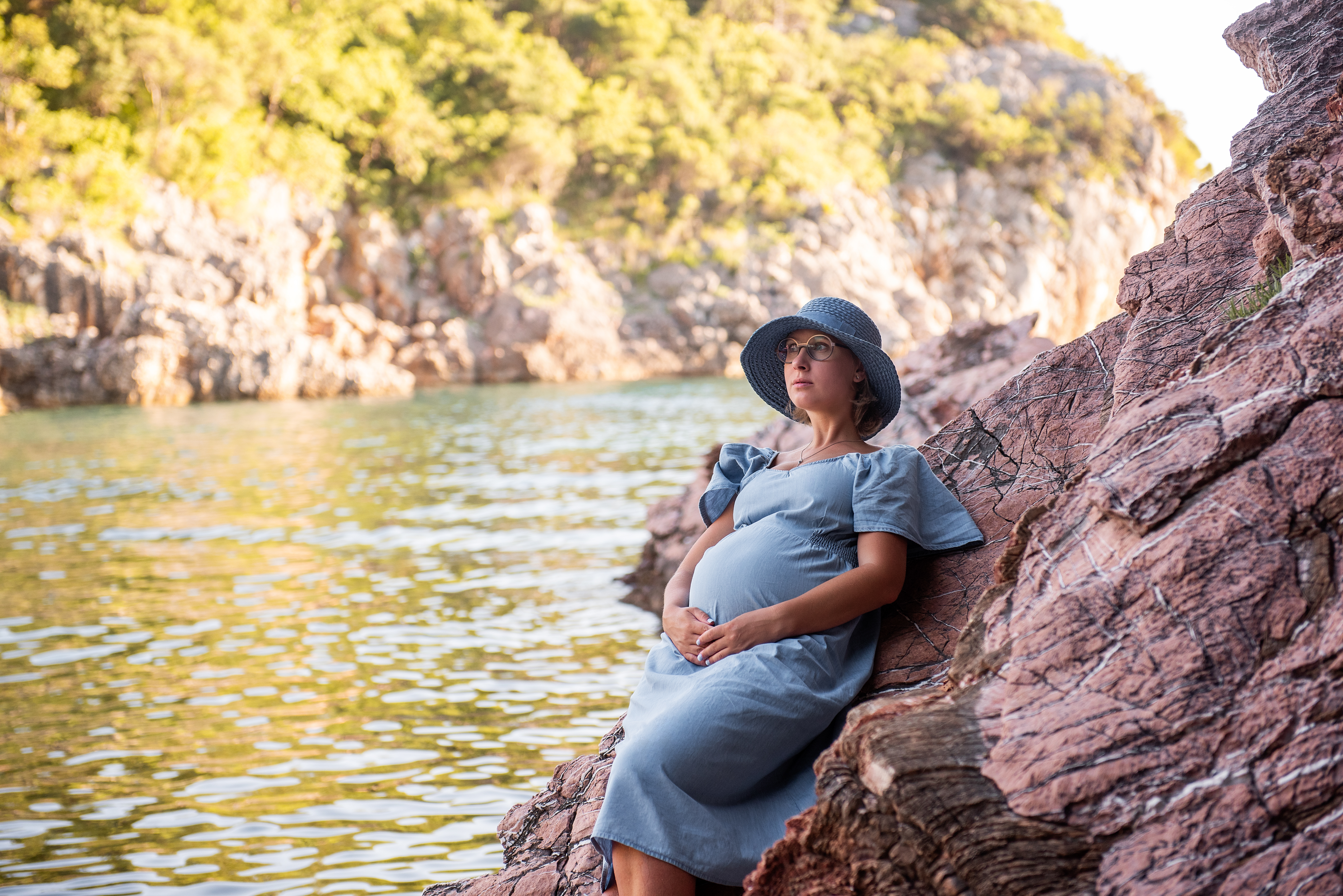 Middle aged pregnant woman sits on rock by the sea. Millennial girl travels in pregnancy on vacation Middle aged pregnant woman sits on rock by the sea. Millennial girl travels in pregnancy on vacation