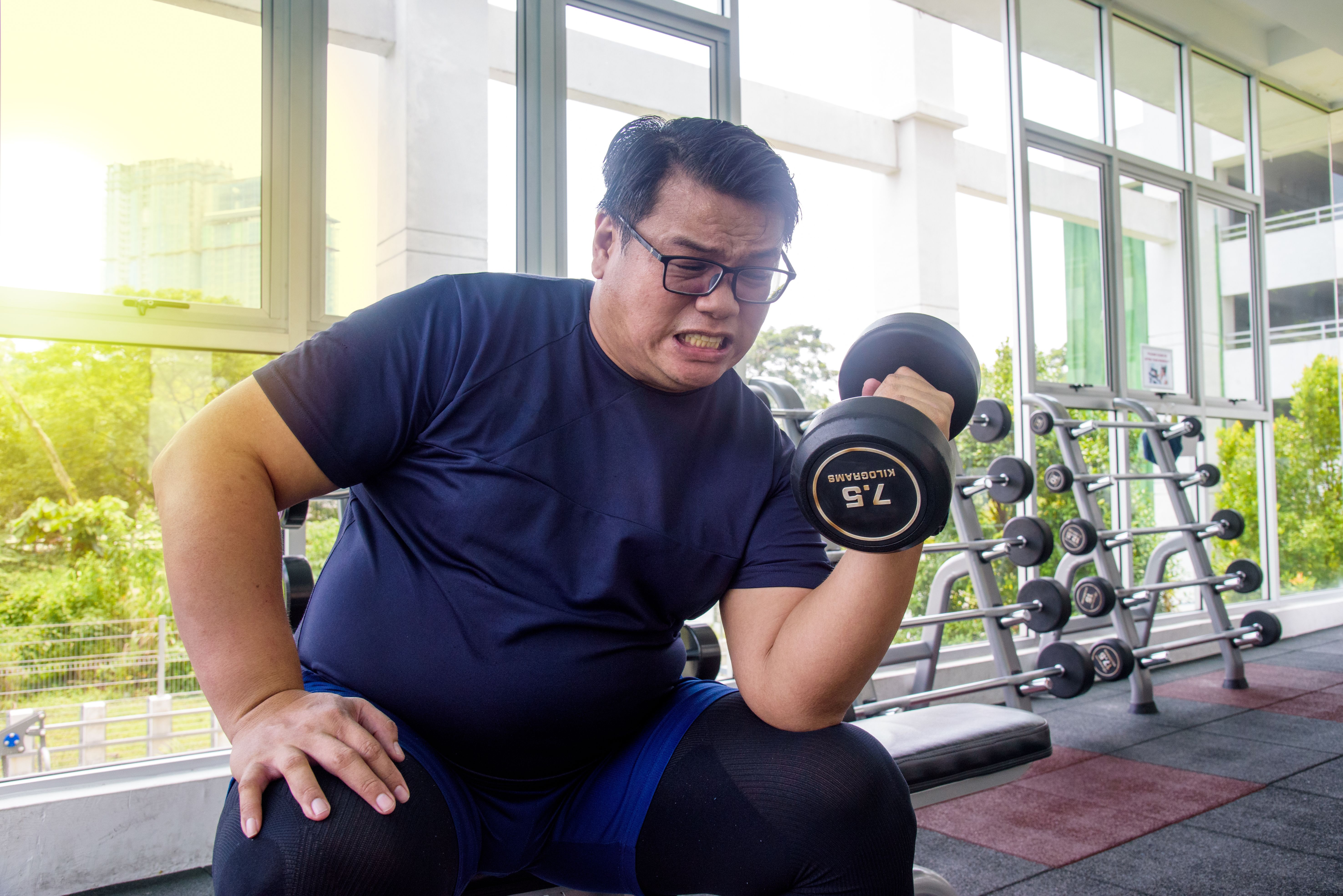 Asian chubby man sitting on bench and holding dumbbell Asian chubby man sitting on bench and holding dumbbell