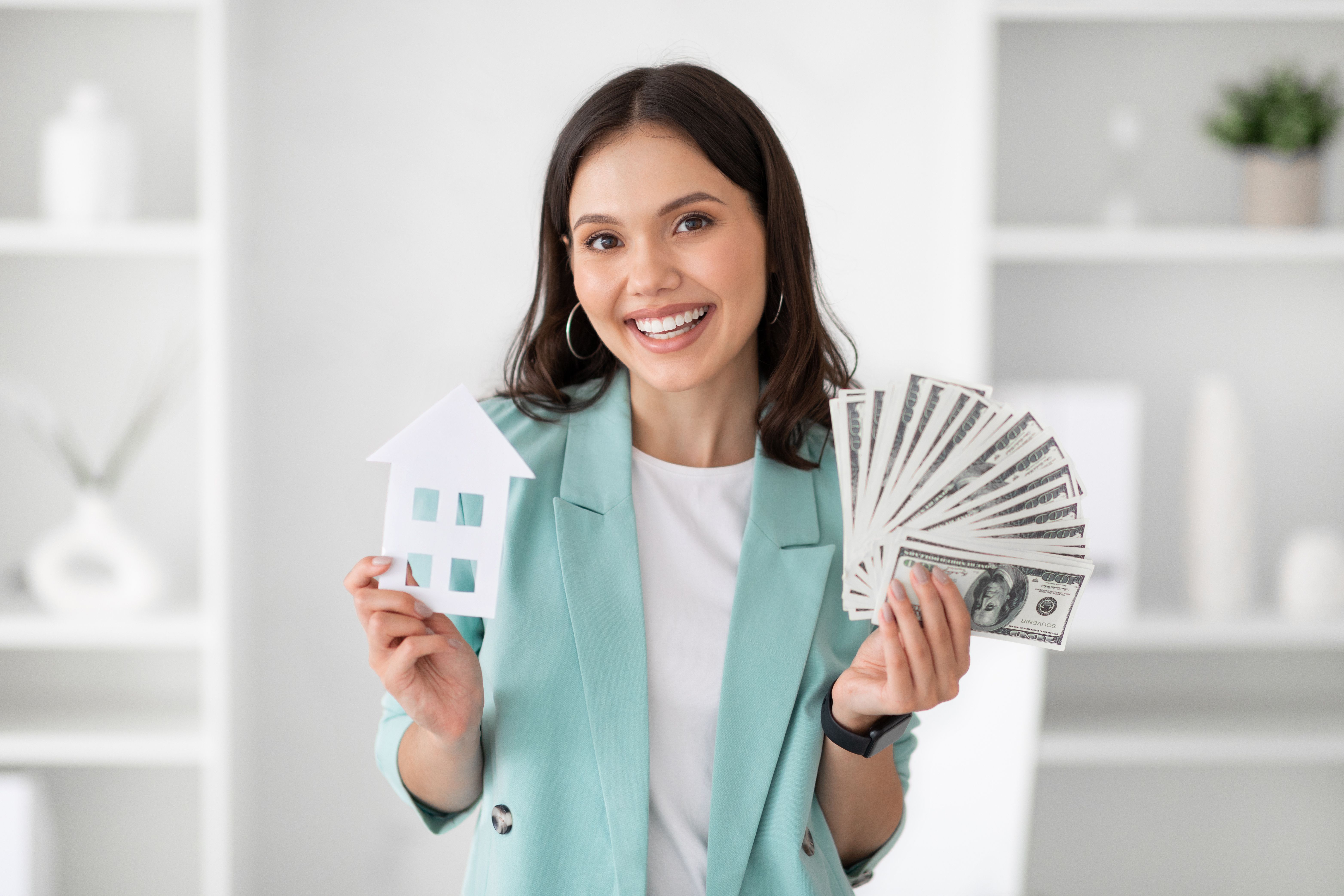 Smiling millennial caucasian lady manager in suit hold a lot of dollars cash and house
