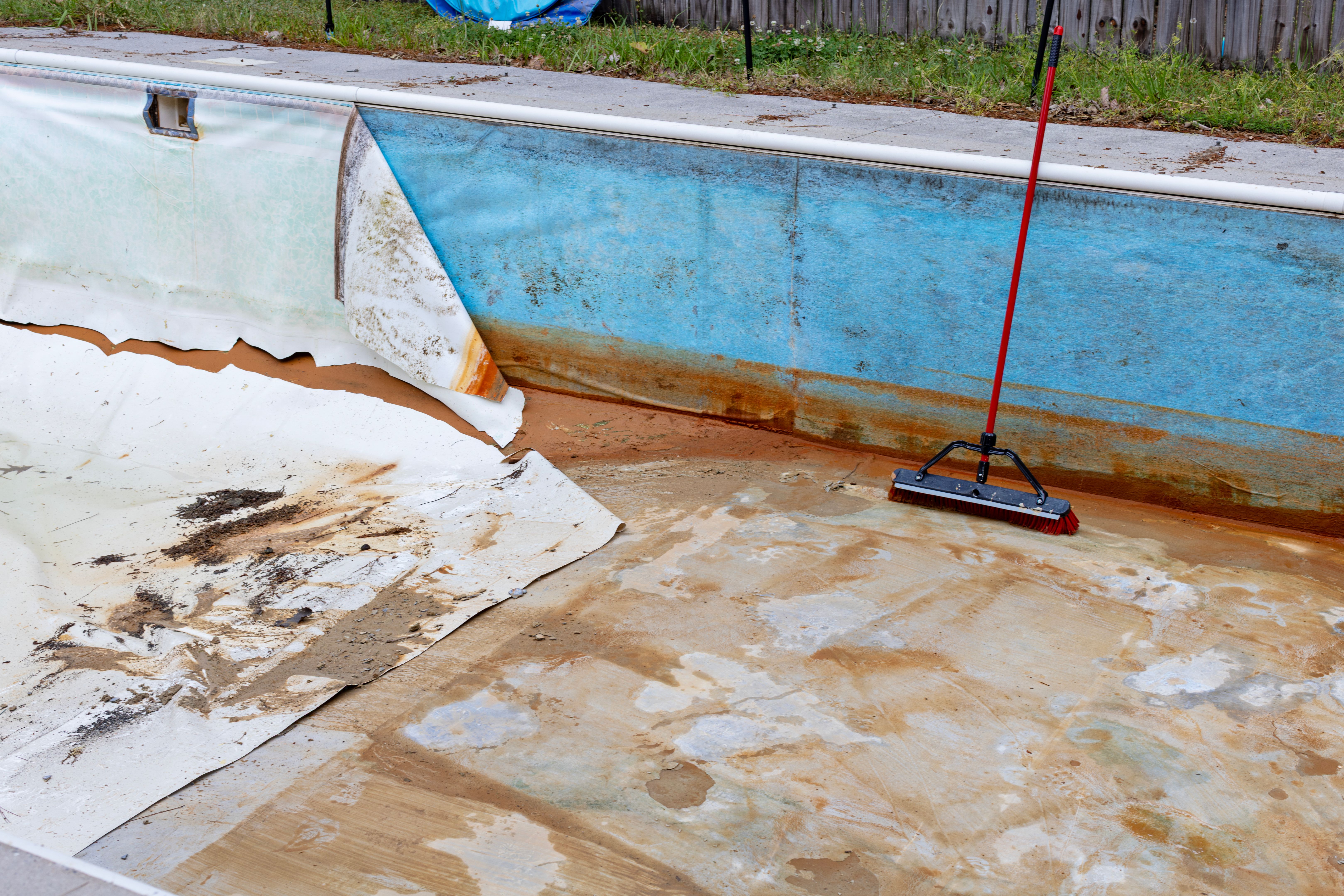 Broom propped in swimming pool in need of a new liner