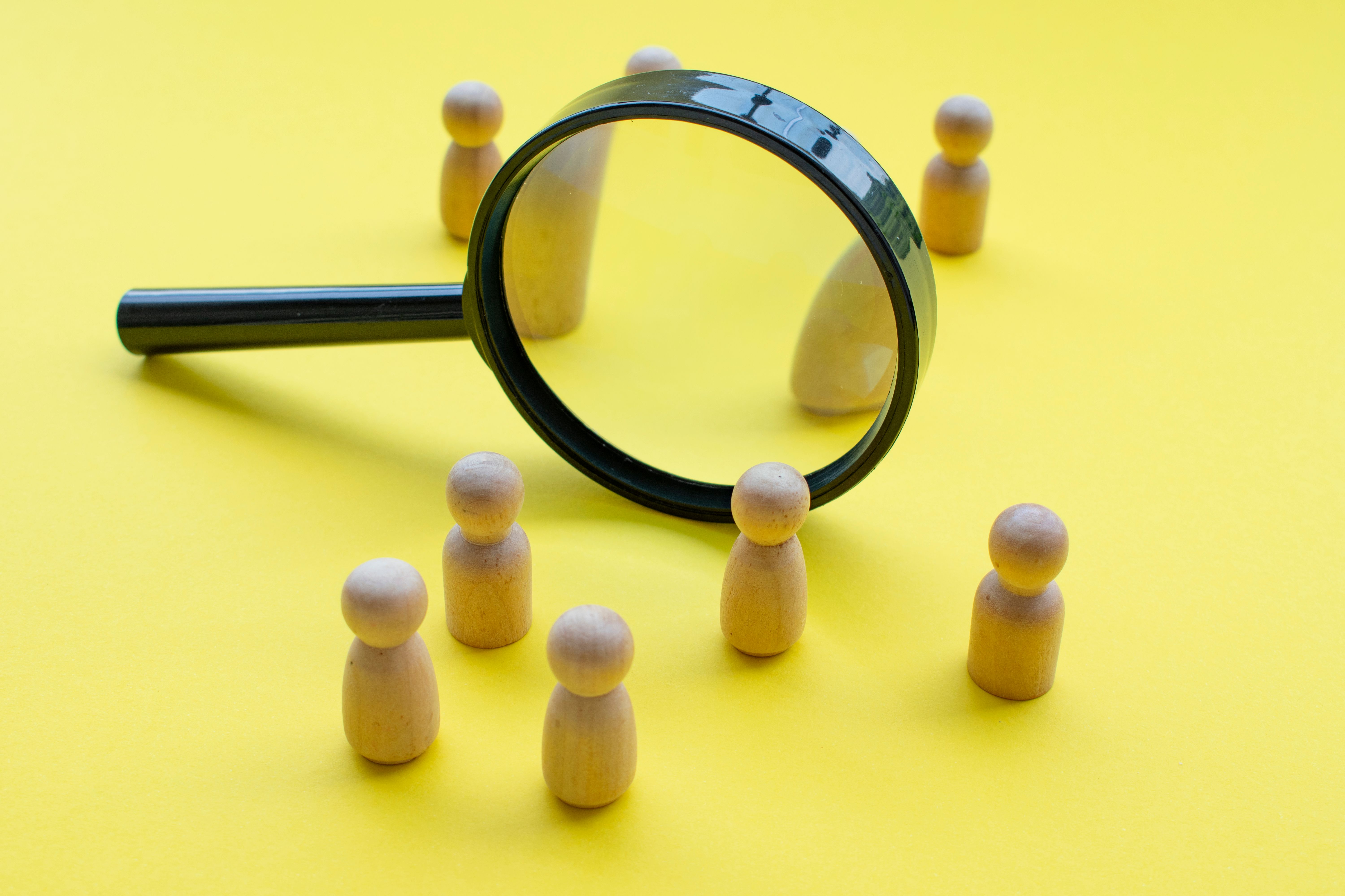 Magnifying glass surrounded by wooden figures. This can represent searching for job, or group discussion or business meeting