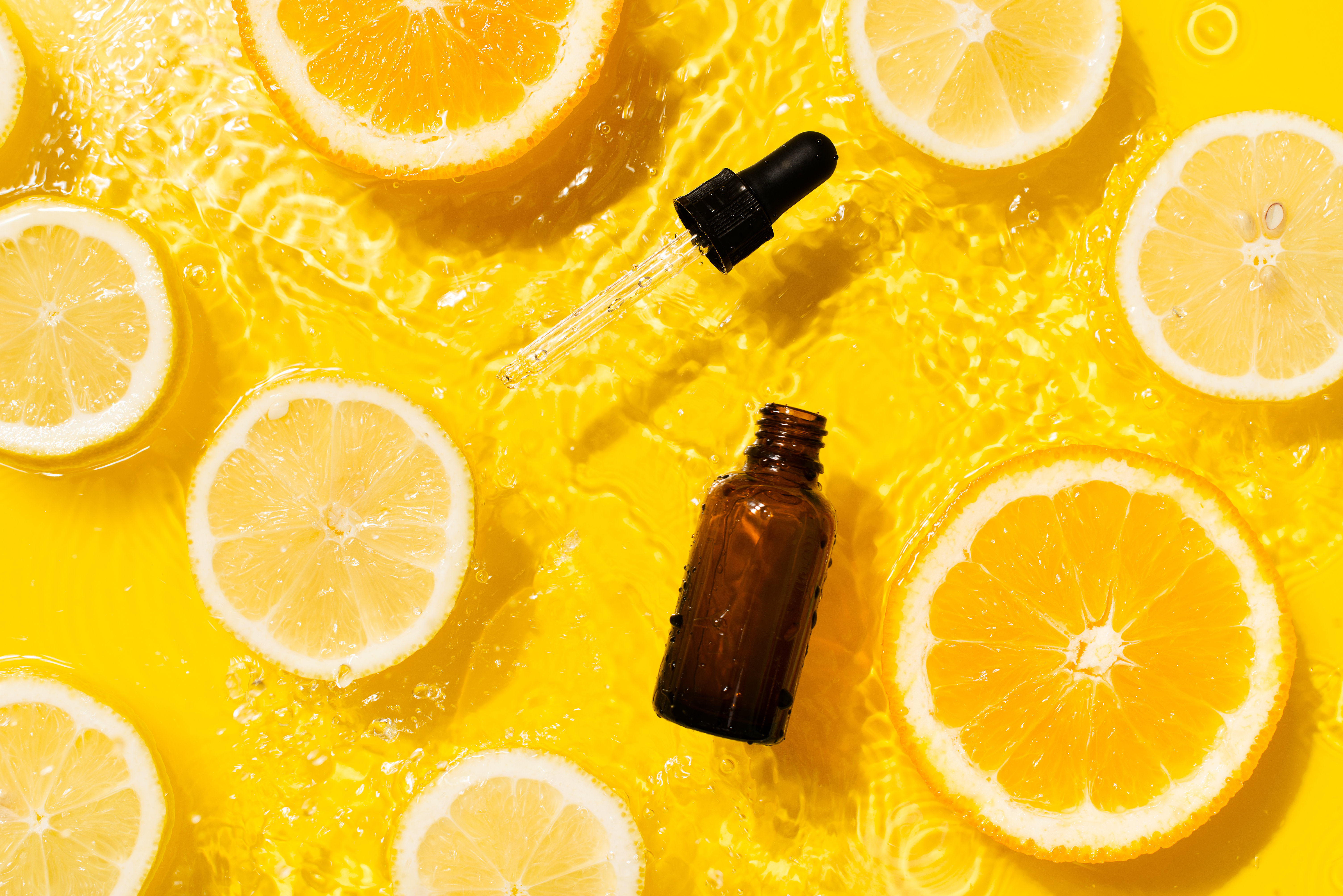 Cosmetic bottle product serum vitamin C with orange and lemon flat lay on yellow background clean water splashing Cosmetic bottle product serum vitamin C with orange and lemon flat lay on yellow background clean water splashing