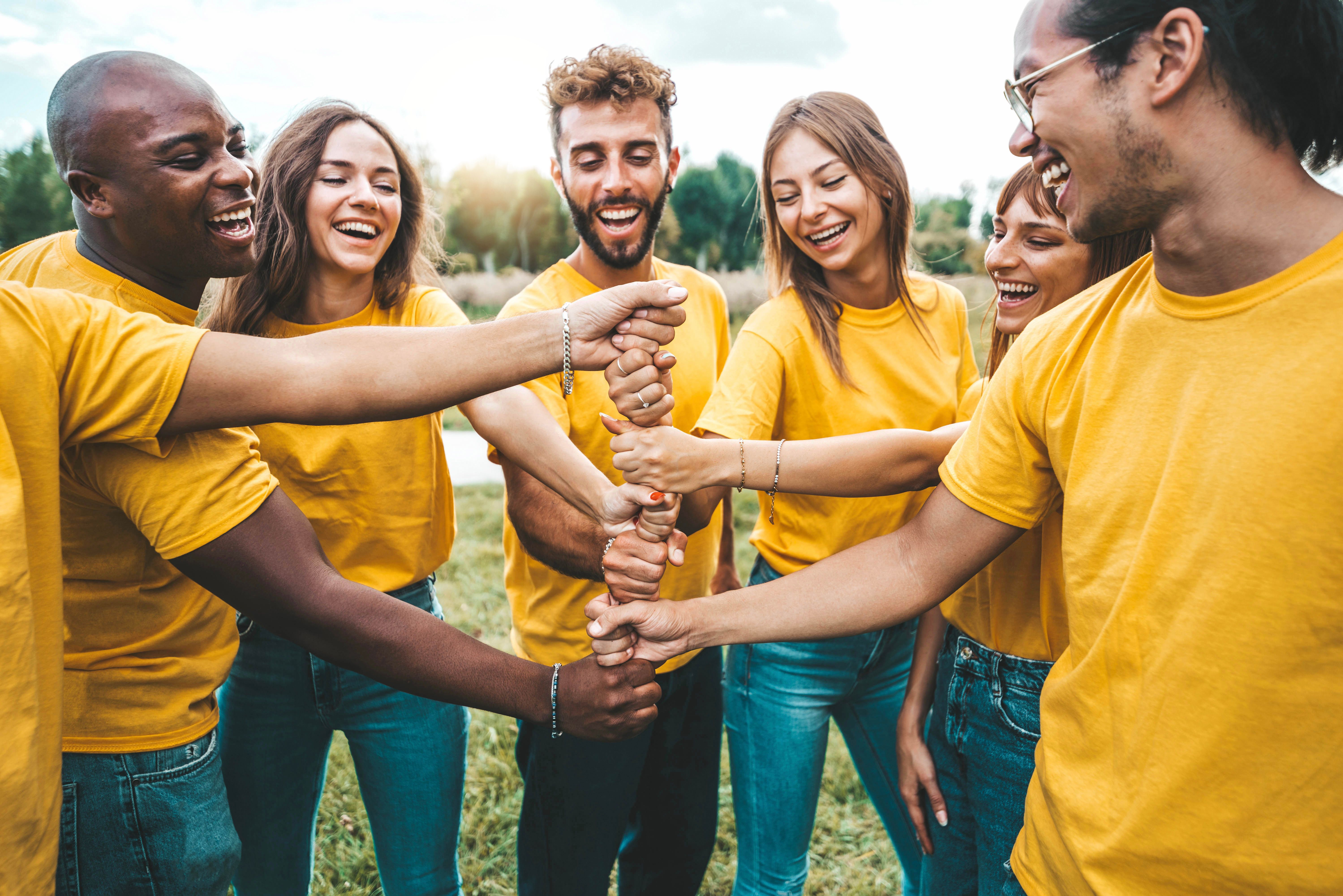 Multiracial happy young people stacking hands outside - University students hugging in college campus - Youth community concept with guys and girls standing together supporting each other
