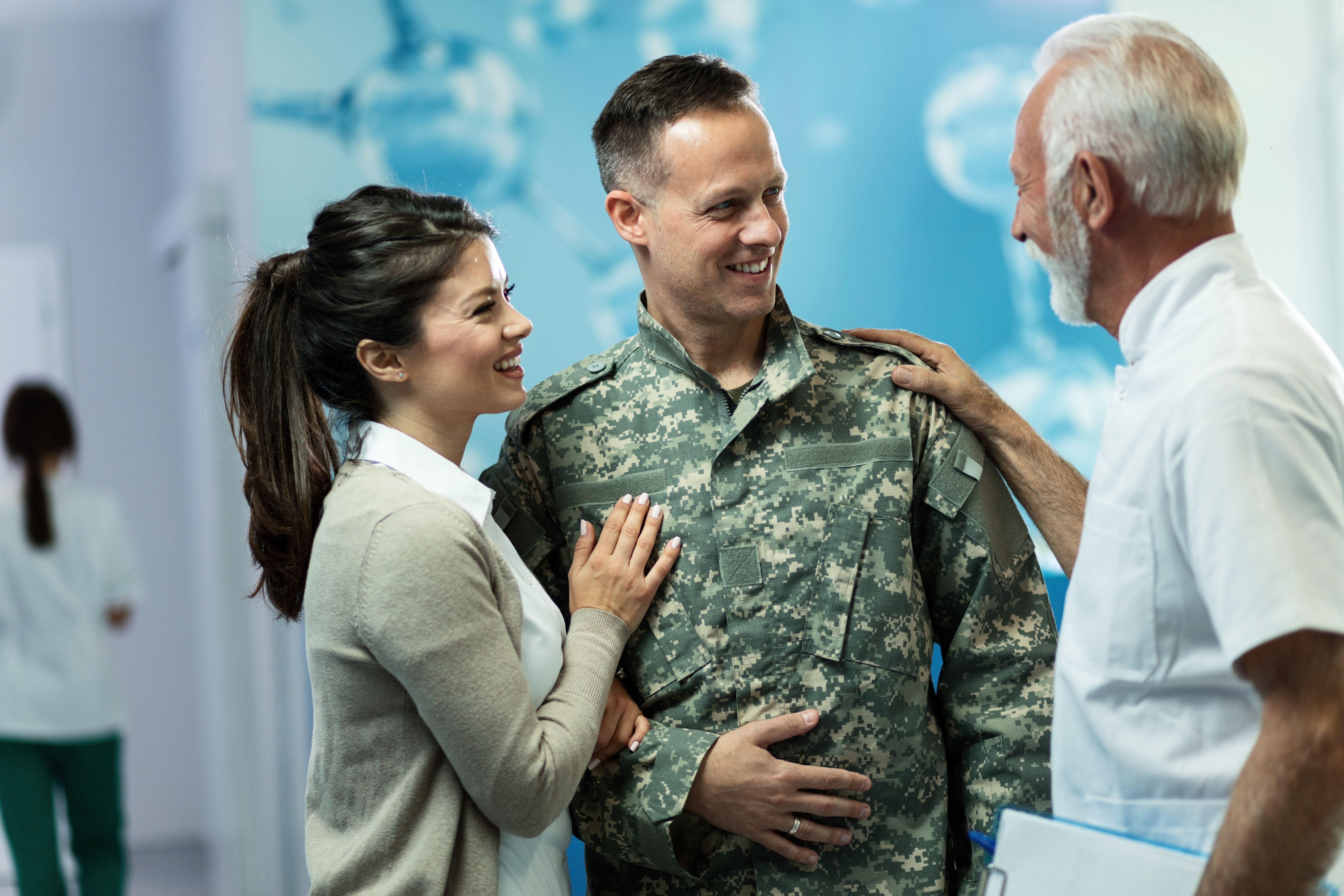 Happy military officer and his wife talking to a doctor in a hallway at clinic.