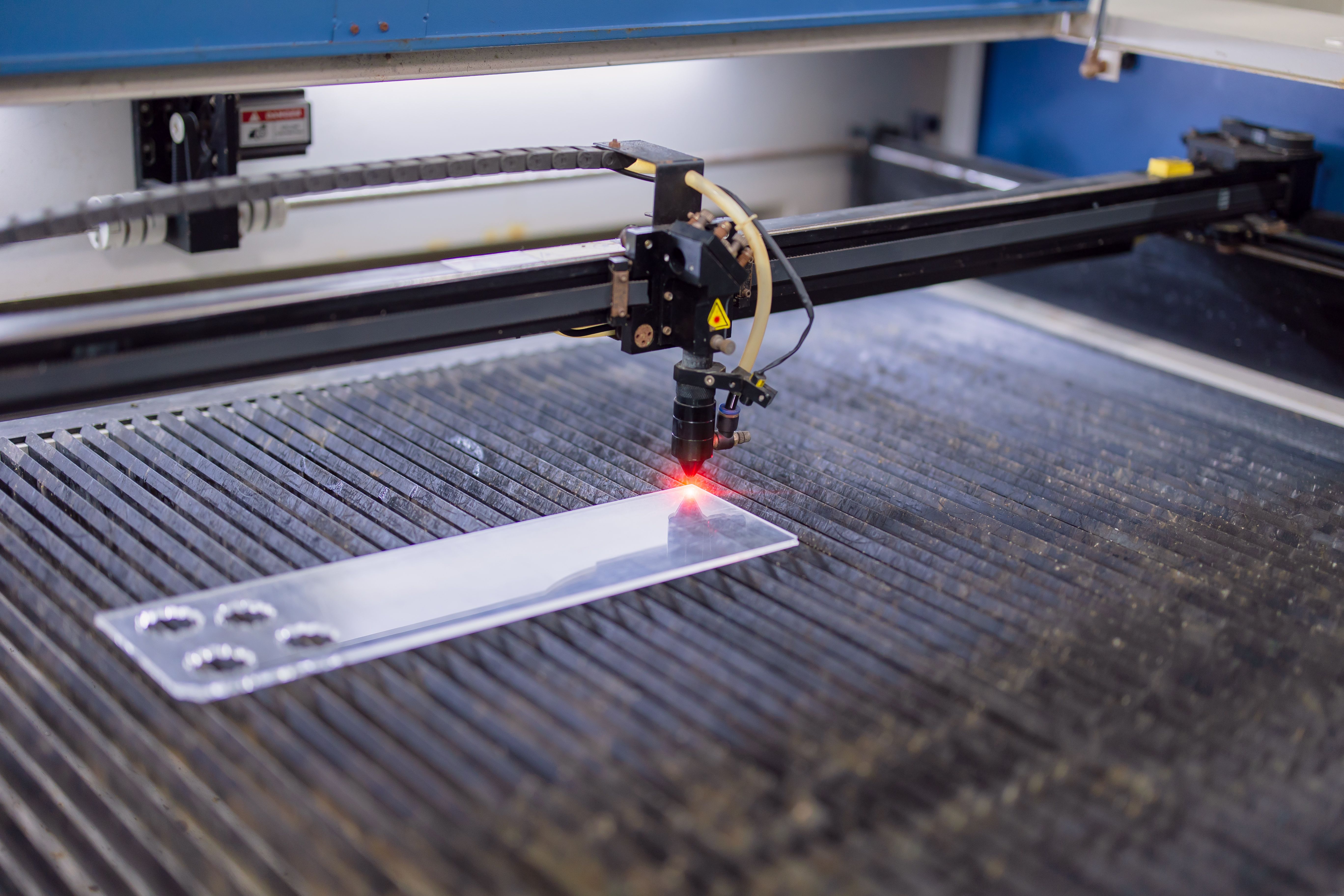 Closeup industrial CO2 laser cutting machine working with high powered red laser beam on acrylic or glass plate