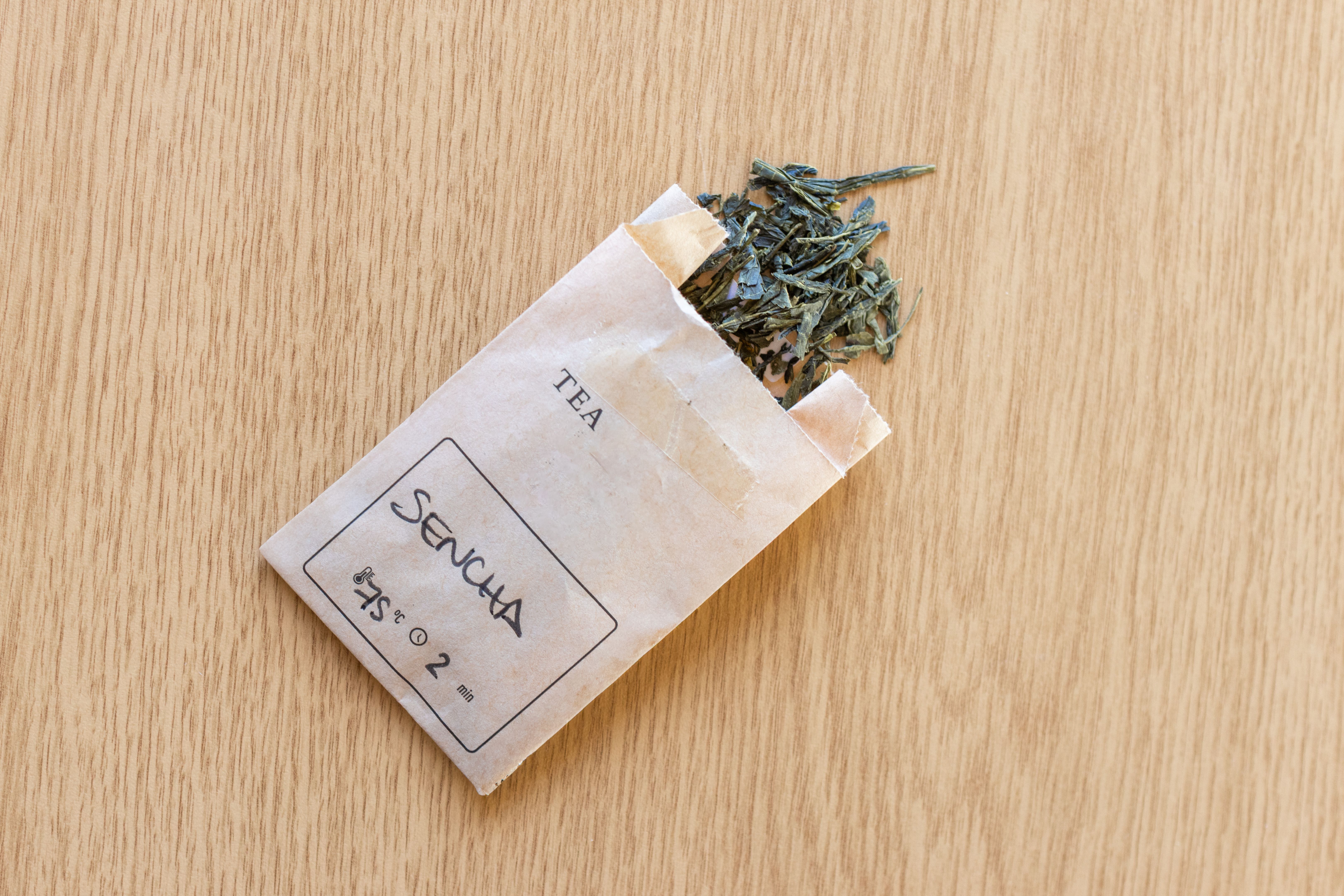Sencha green tea leaves spilling from paper bag on wooden table