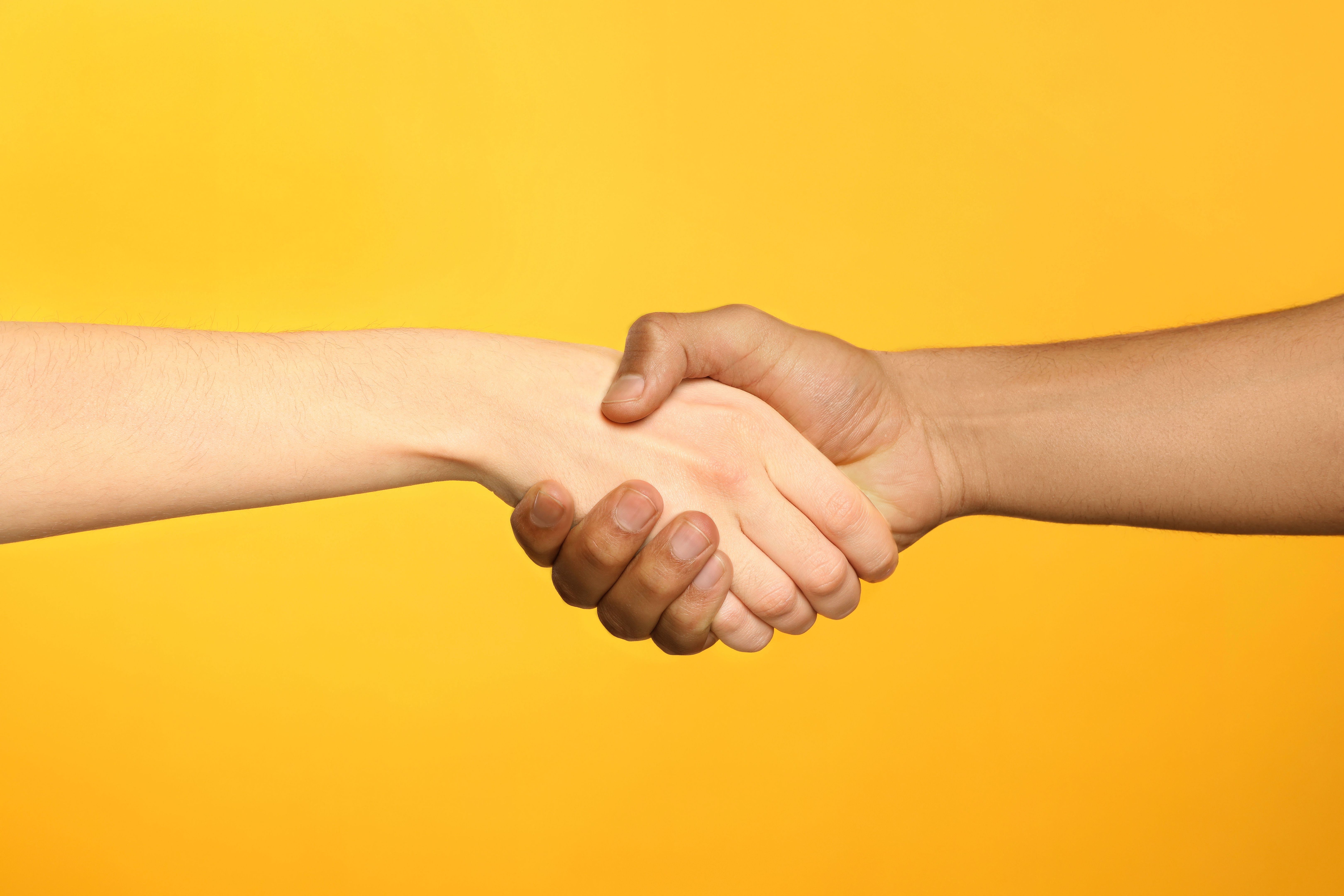 International relationships. People shaking hands on orange background, closeup International relationships. People shaking hands on orange background, closeup