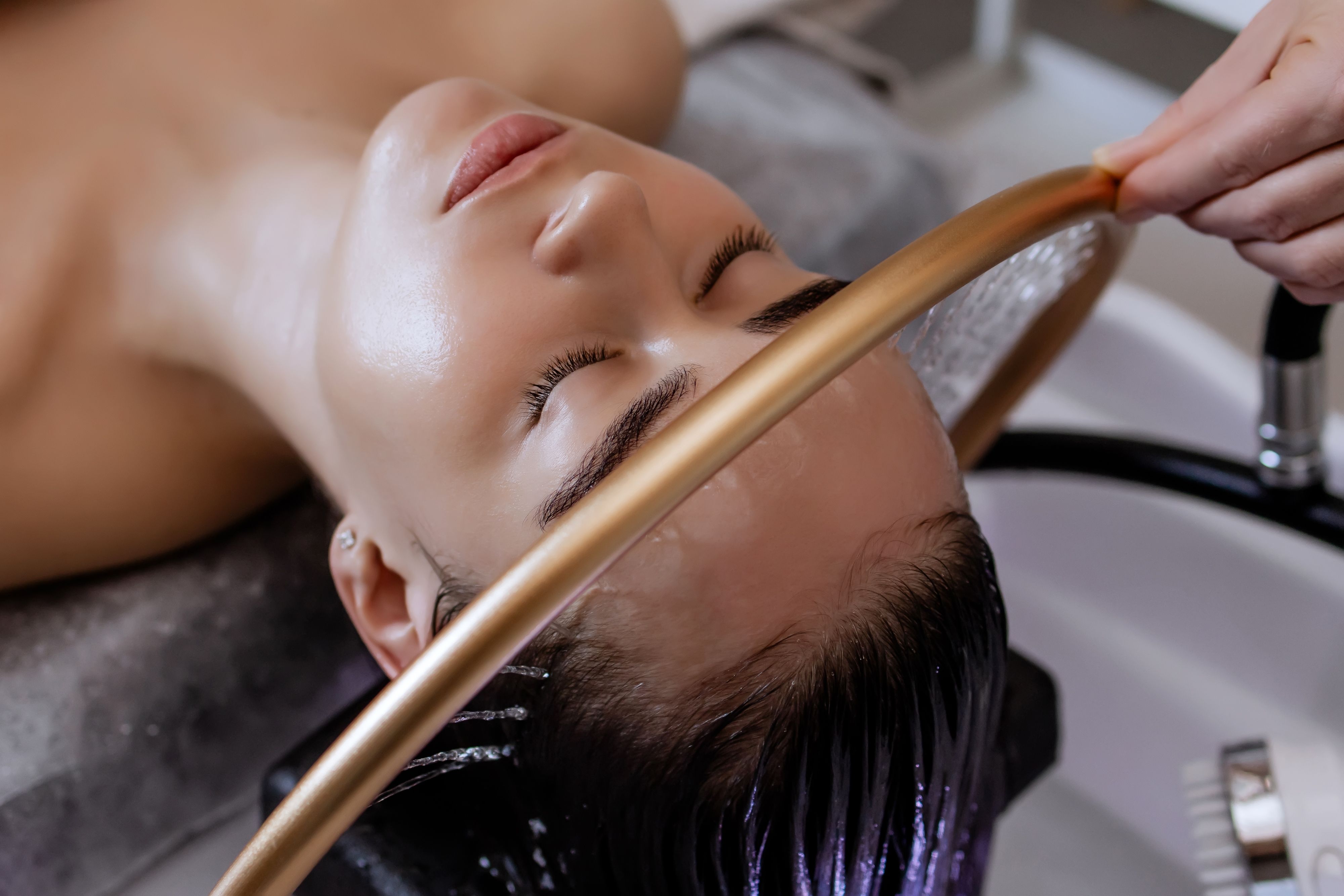 Close-up of a woman receiving a head massage during a Japanese head spa treatment with water flowing from a special hair washing tool, focusing on the scalp relaxation and beauty therapy