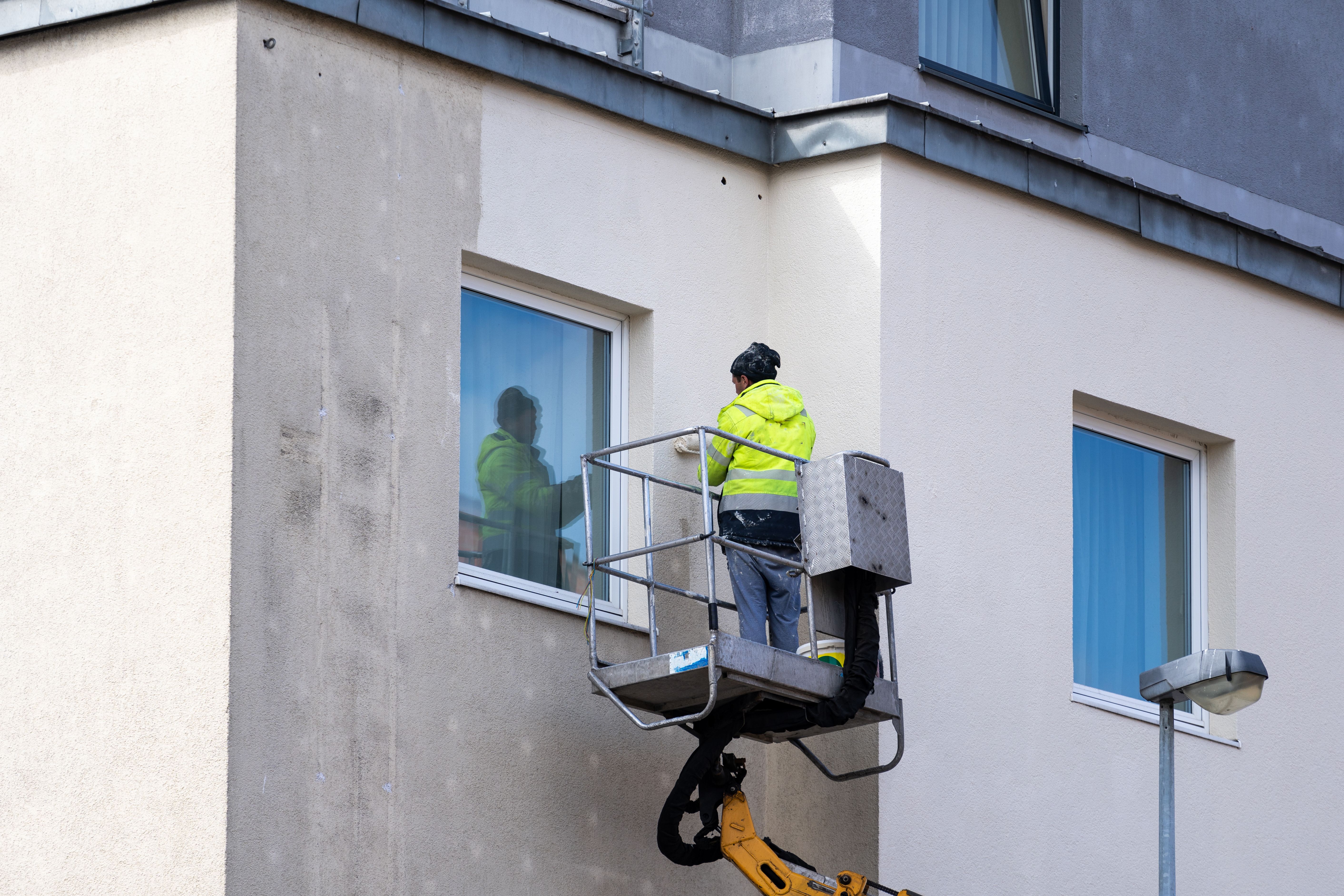 Maintenance worker using roller brush paints the facade of a residential house