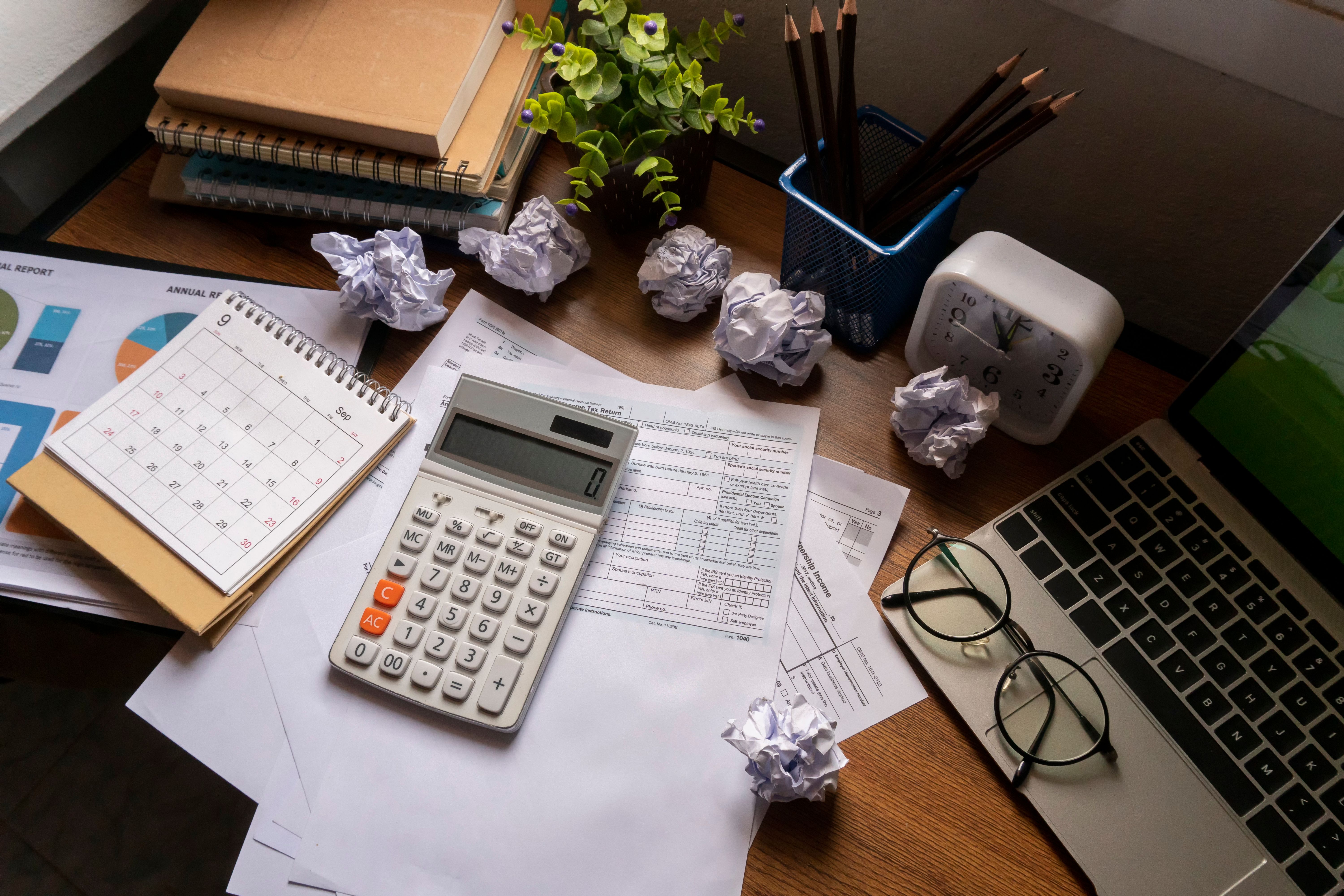 Home Office Desk Concept. Laptop, and calculator for accountant or bookkeeper plan annual budget report and tax. Computer, Crumpled paper, and pencil placed on wooden table. Home Office Desk Concept. Laptop, and calculator for accountant or bookkeeper plan annual budget report and tax. Computer, Crumpled paper, and pencil placed on wooden table.