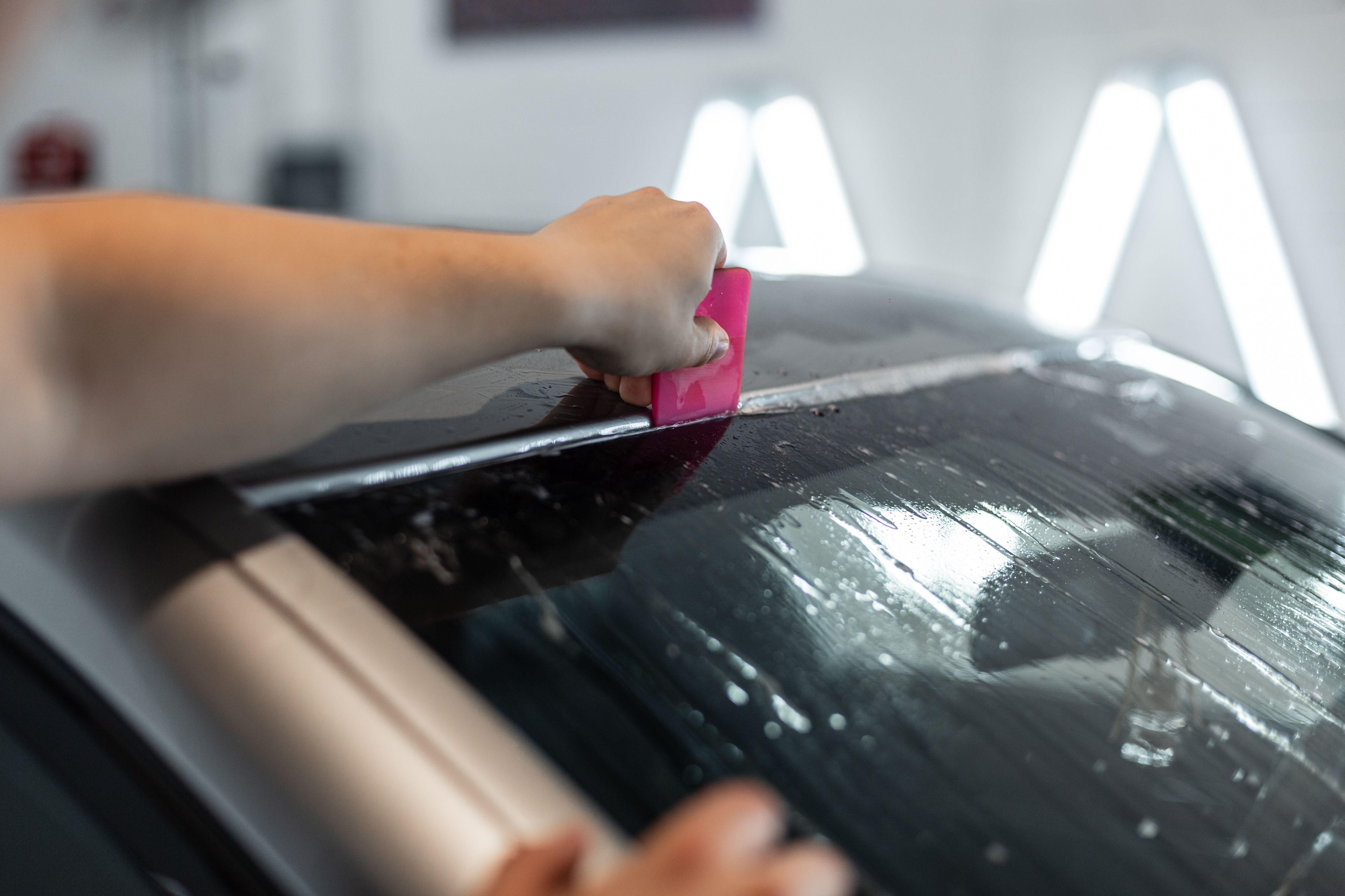 A professional man applies protective film to a car in a detailing center