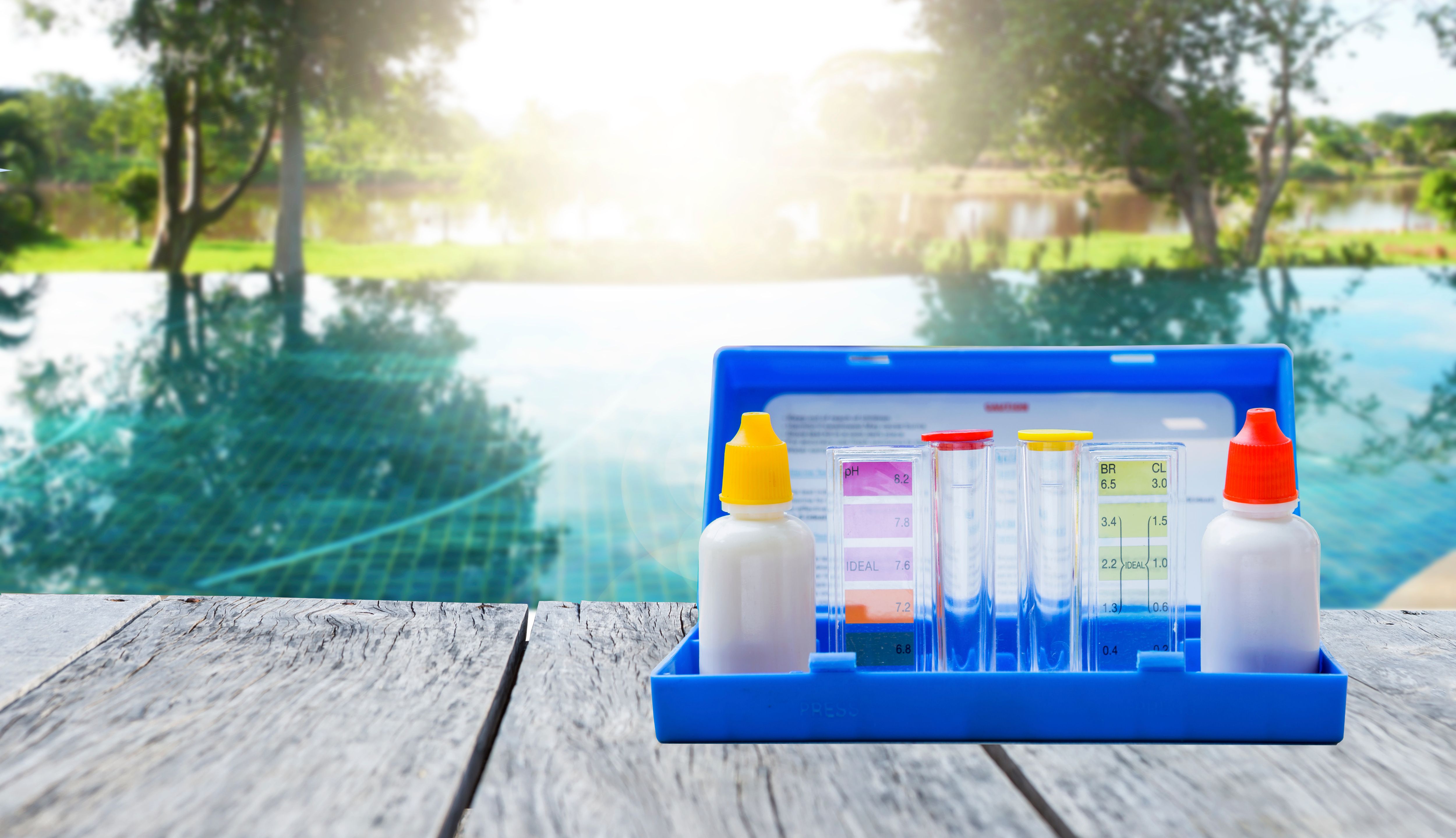 Water tester test kit on wooden table over blurred resort swimming pool background