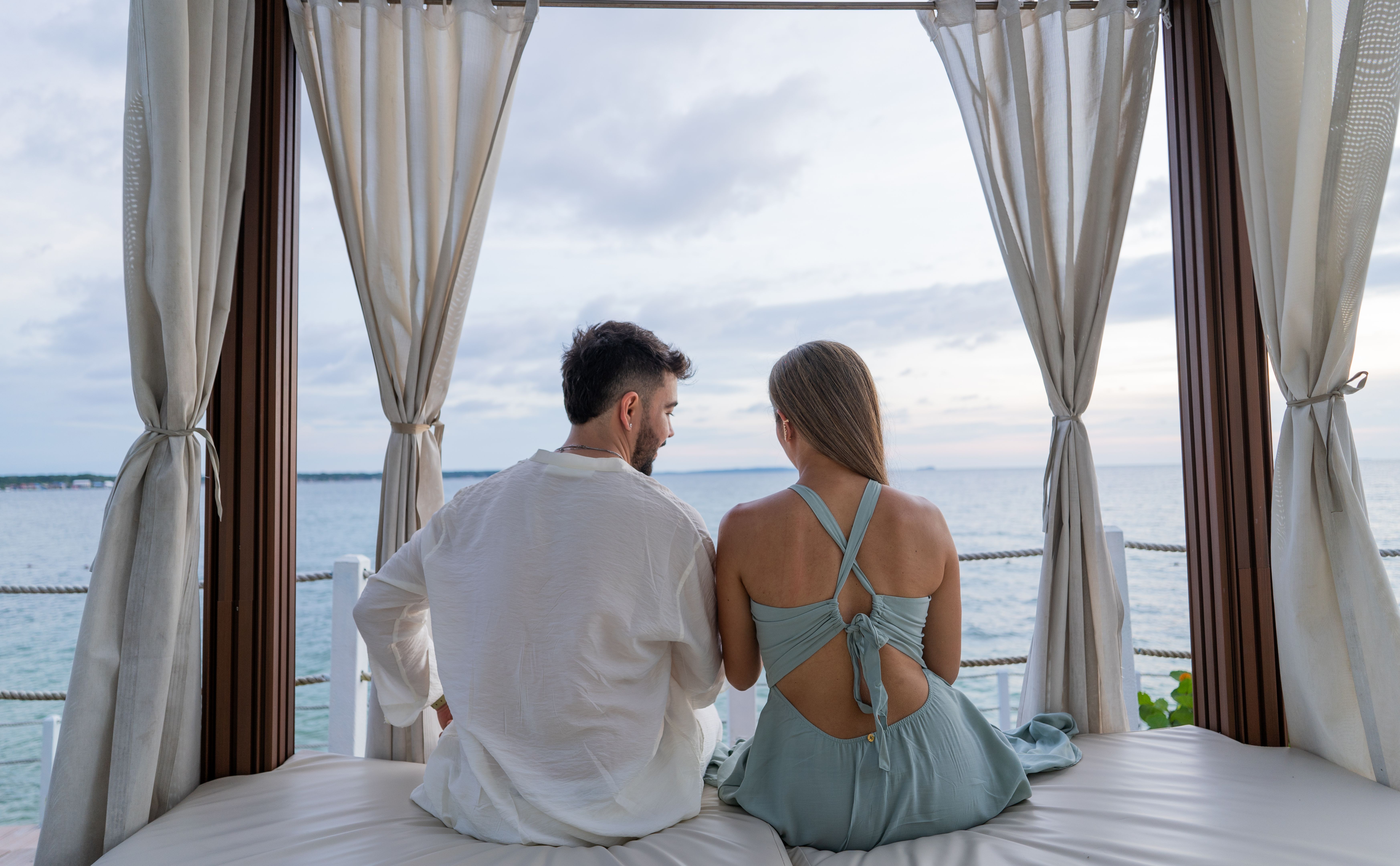 couple on their backs sitting on bed on hotel veranda overlooking the sea - stock photo