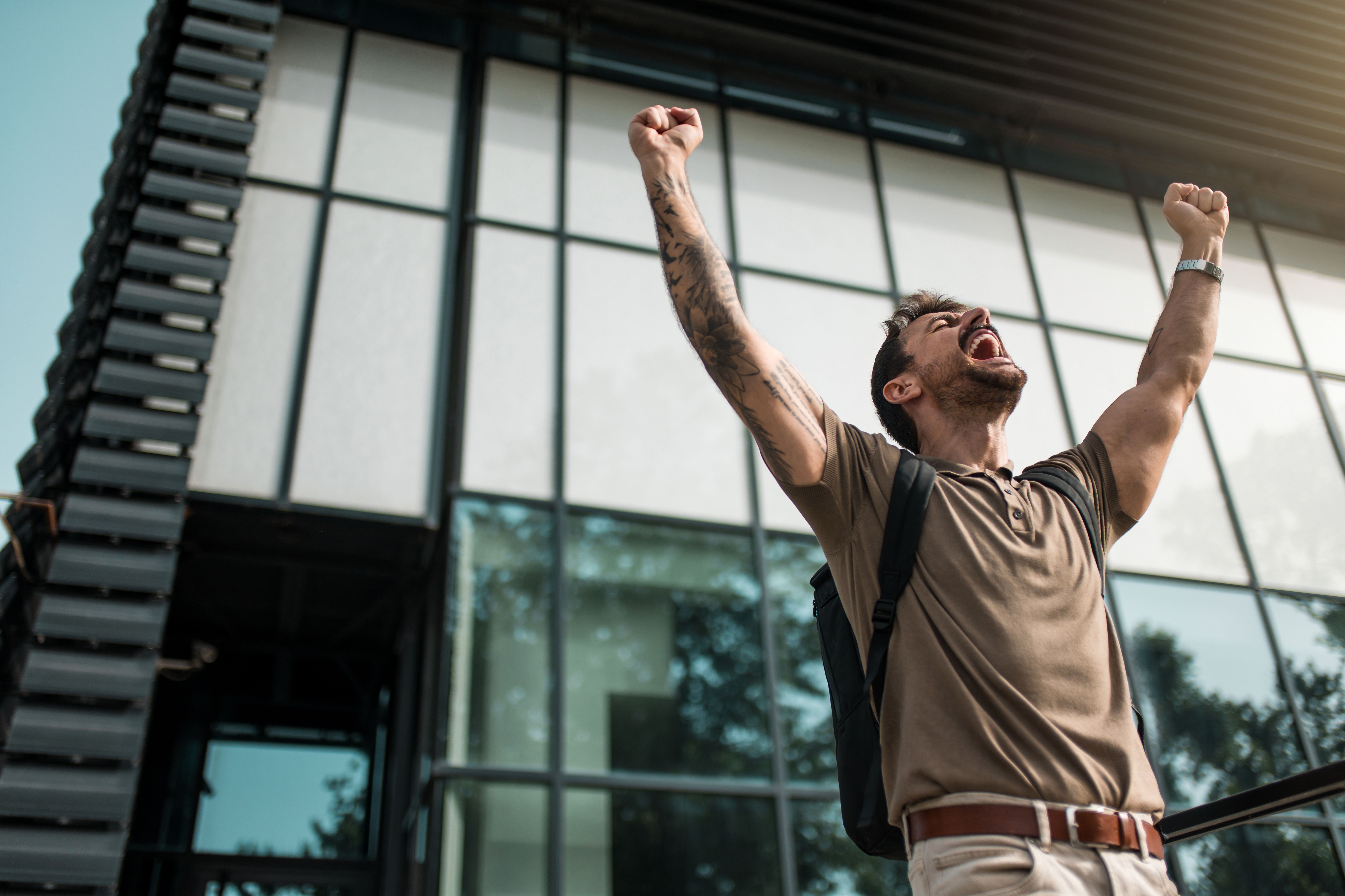 Ecstatic young man celebrating success while standing in front of an office building.