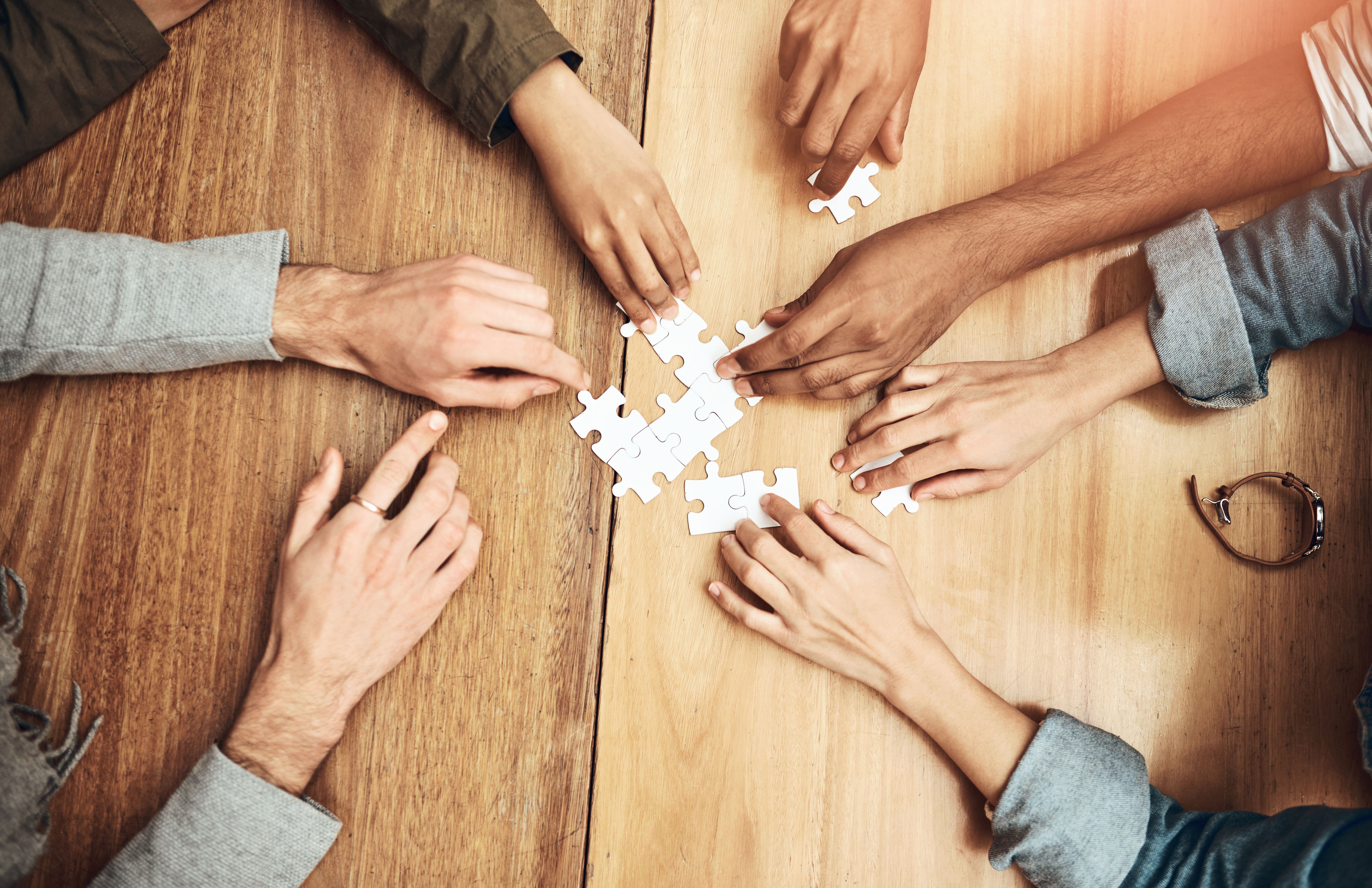 Puzzle, above and hands of business people for teamwork, collaboration and working together. Meeting, diversity and workers with jigsaw for problem solving, challenge and cooperation in office