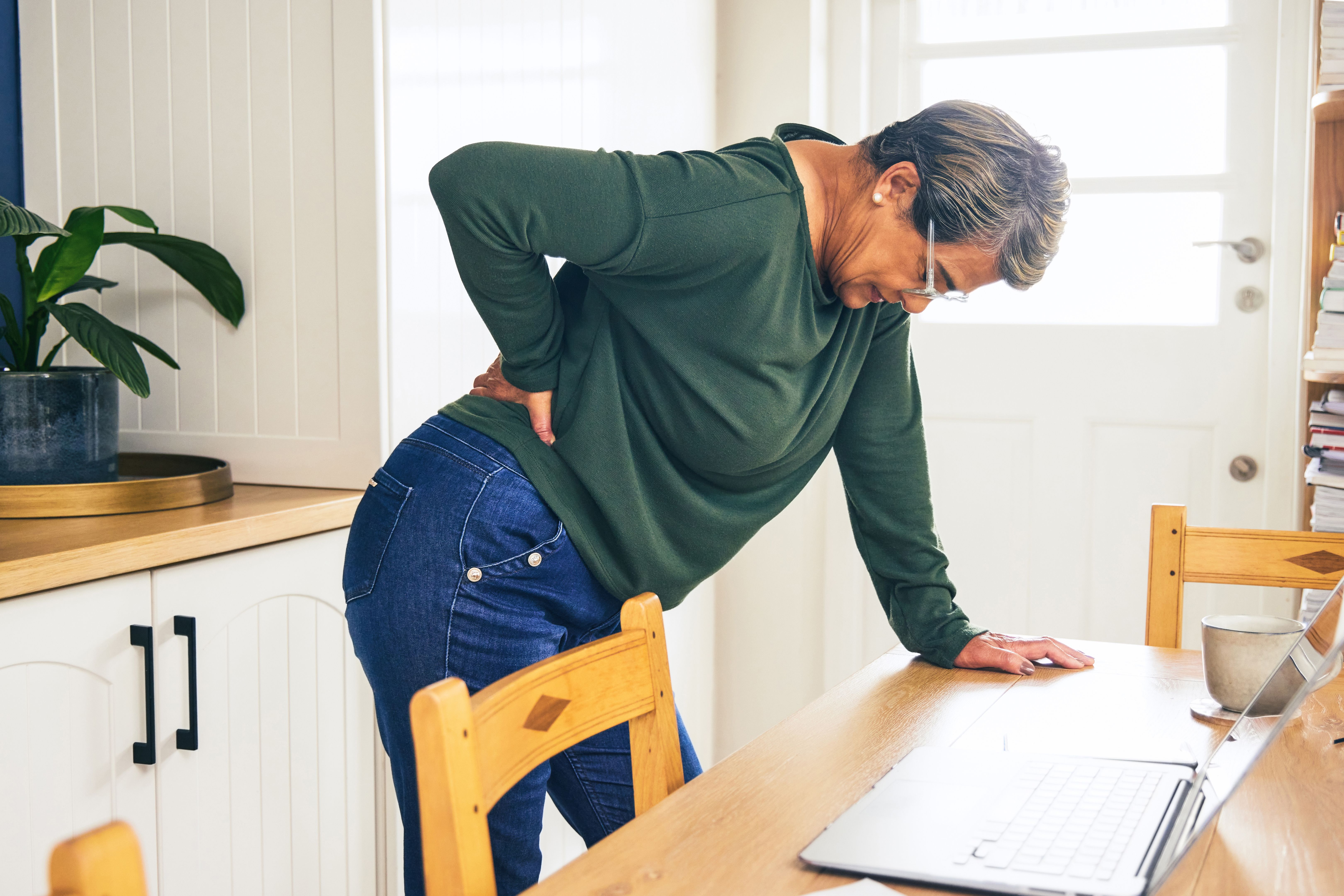 Shot of a mature woman standing and suffering from backache while working from home Shot of a mature woman standing and suffering from backache while working from home