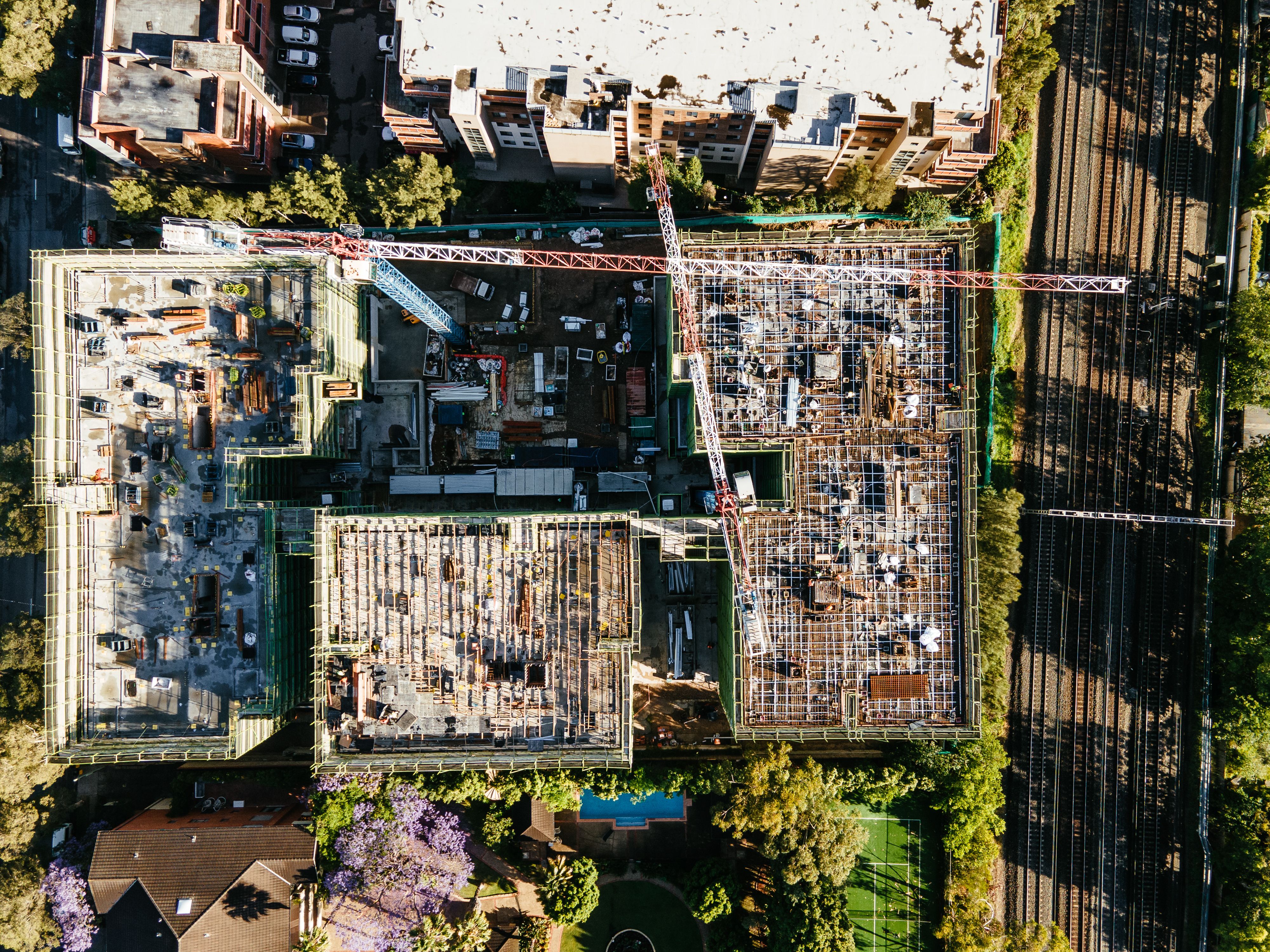 Aerial view of a large construction site with a tower crane towering over the framework surrounded by a suburban landscape