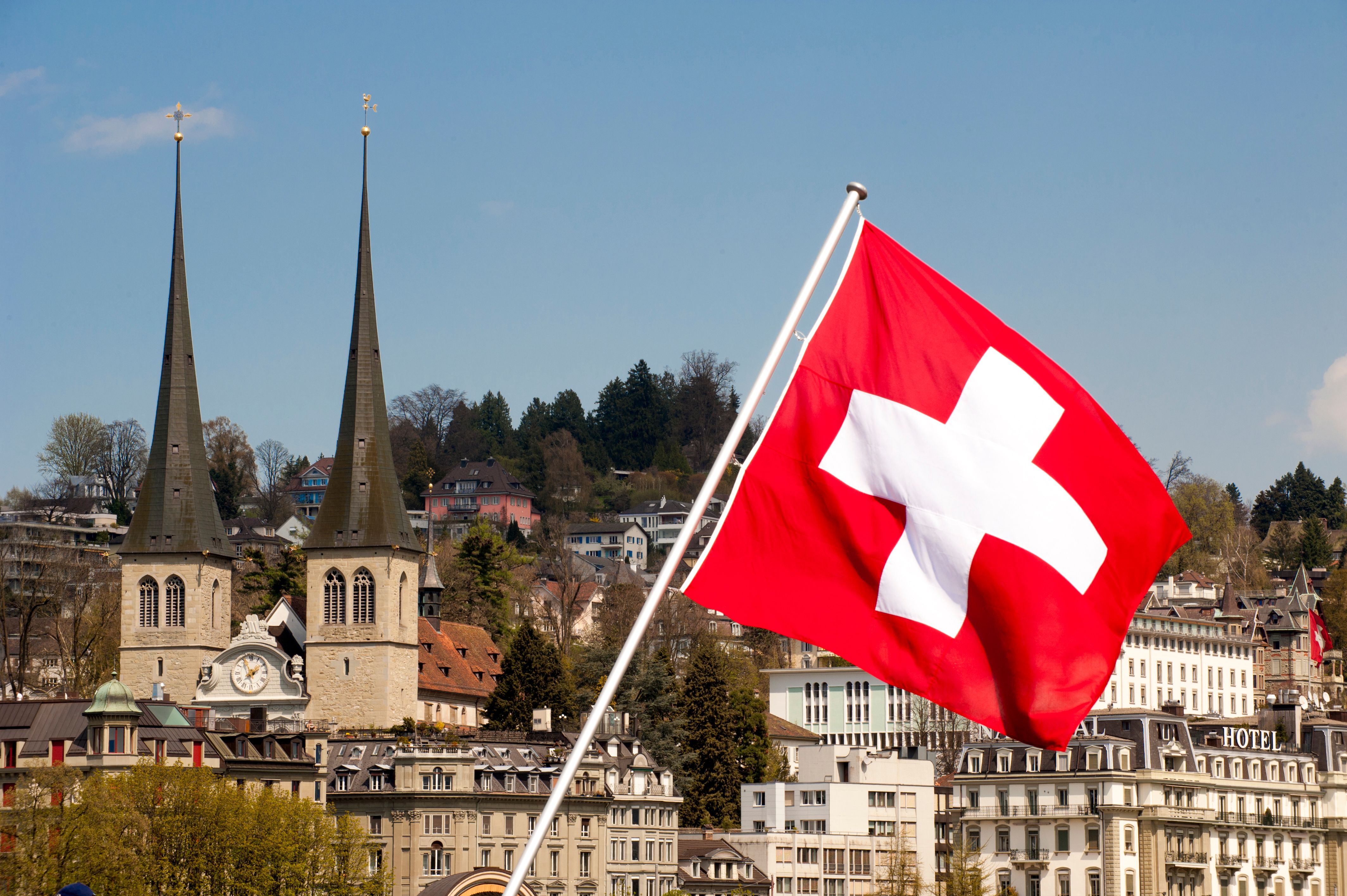 Drapeau national suisse hissé devant les deux tours de l'église Saint-Léger et les hôtels de Lucerne, en Suisse.