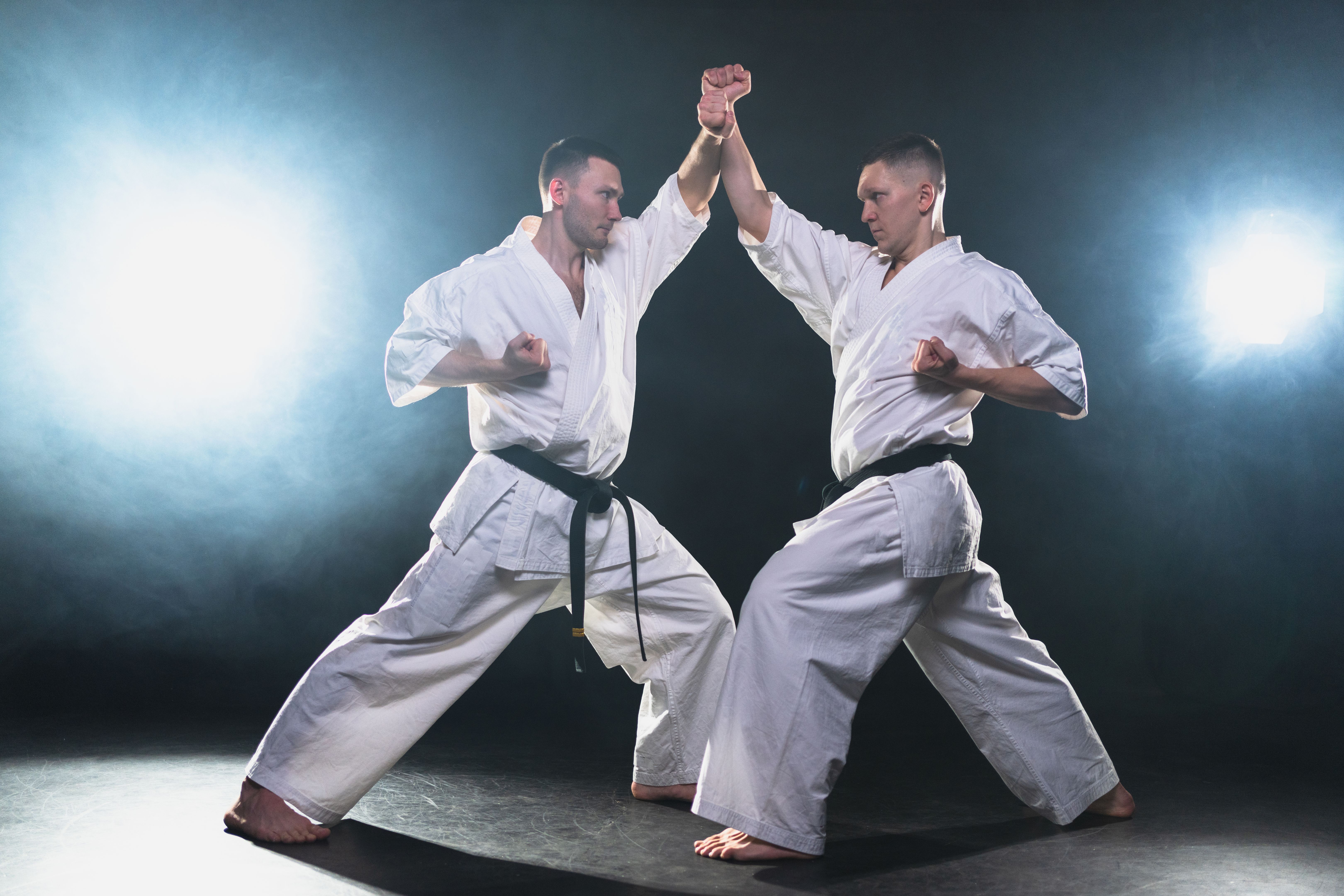 Martial arts masters on dark background. Strong man fighters in white kimono for karate martial arts fighting training in black gym, Karate fighters training punches kicks practicing fight sparring