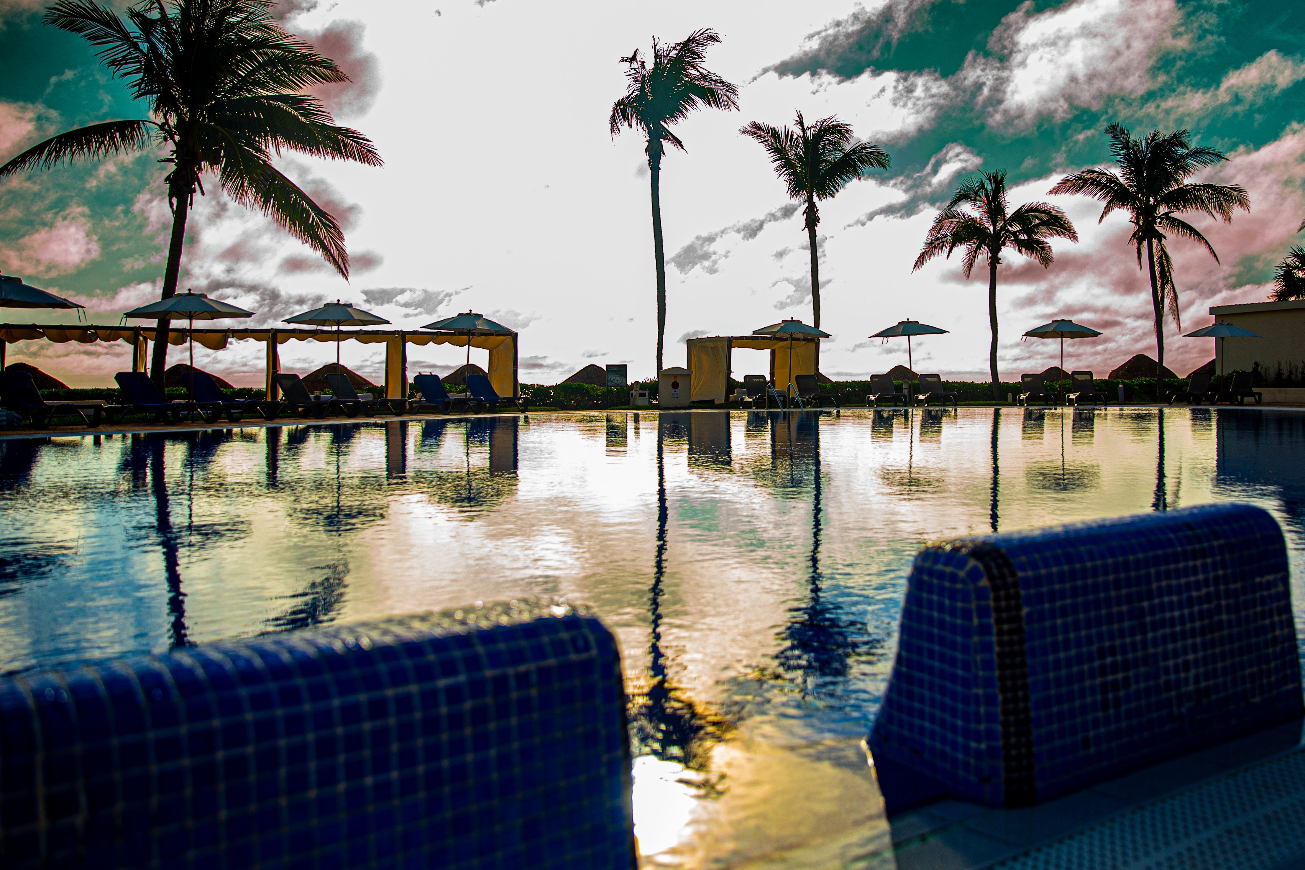 Luxury resort pool at sunset with palm trees, lounge chairs, and cabanas reflecting on the calm water. Luxury resort pool at sunset with palm trees, lounge chairs, and cabanas reflecting on the calm water.