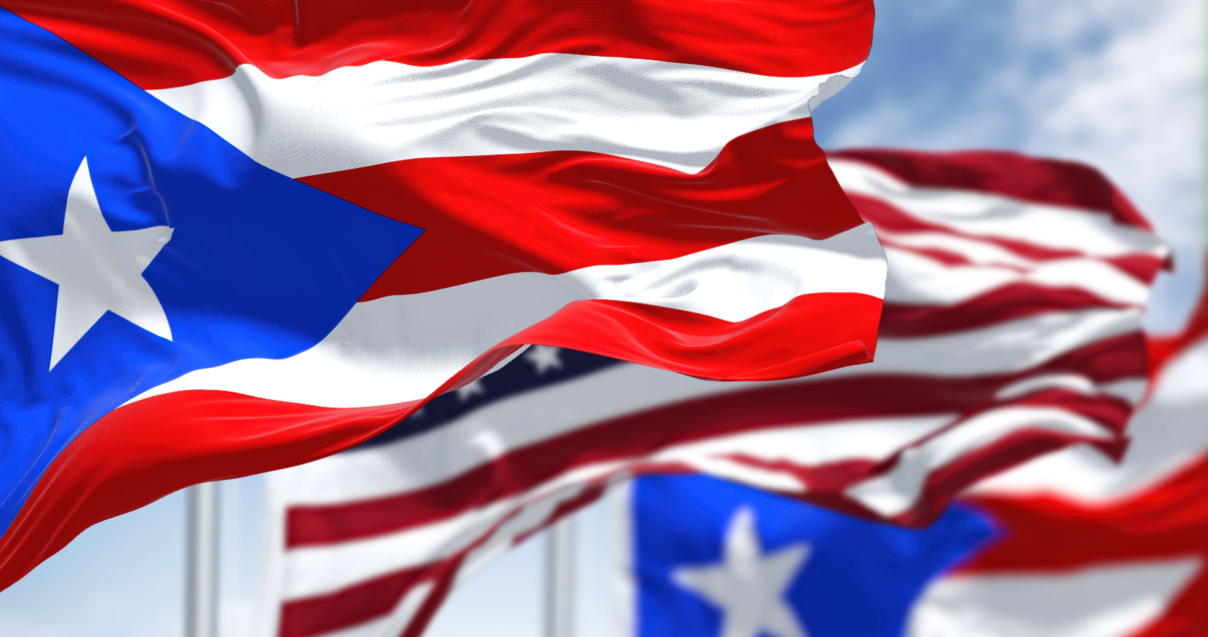 Banderas de Puerto Rico ondeando al viento con la bandera de Estados Unidos en un día despejado