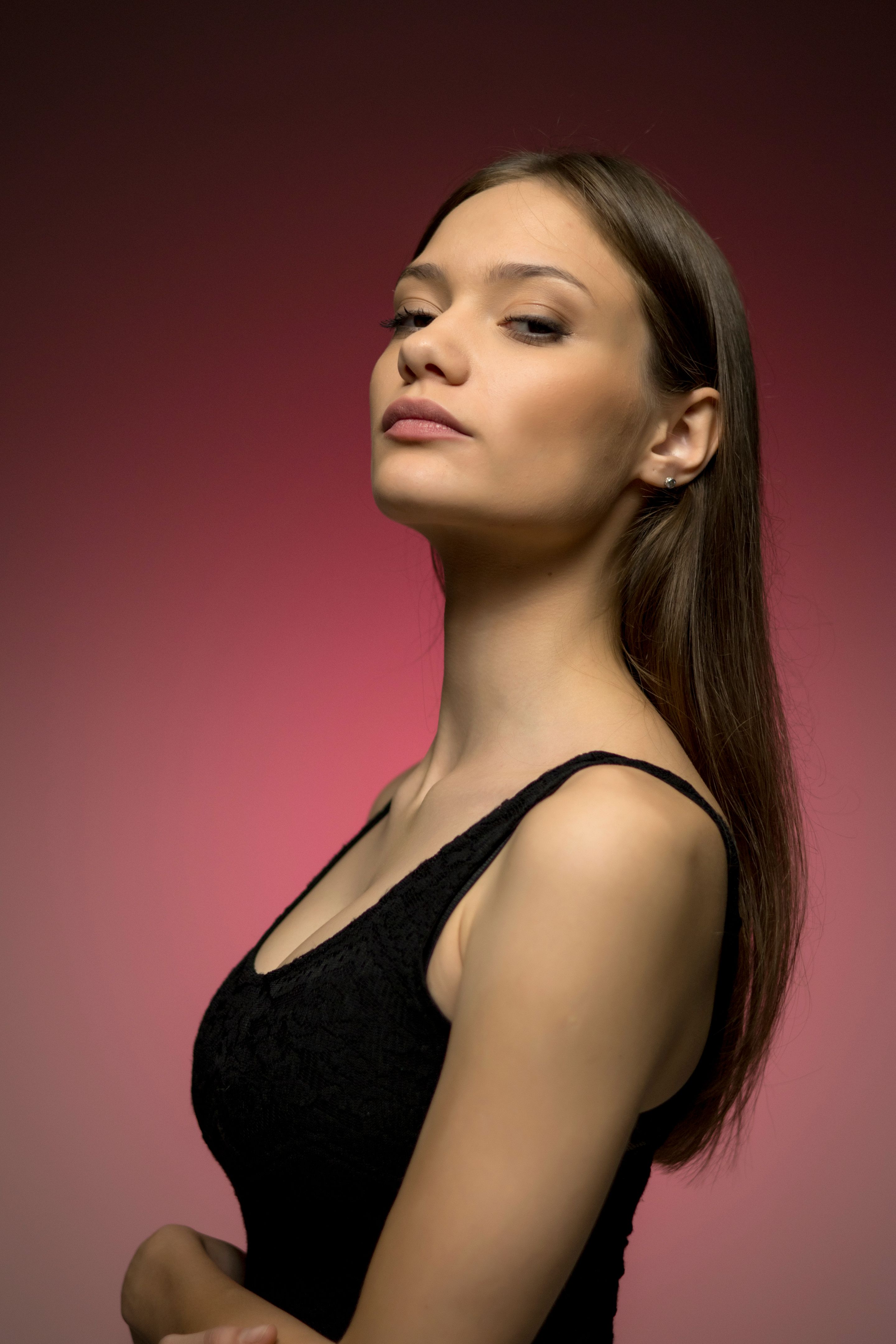 Dramatic upward angle portrait with pink gradient background. Model's confident pose and elegant profile create powerful fashion aesthetic