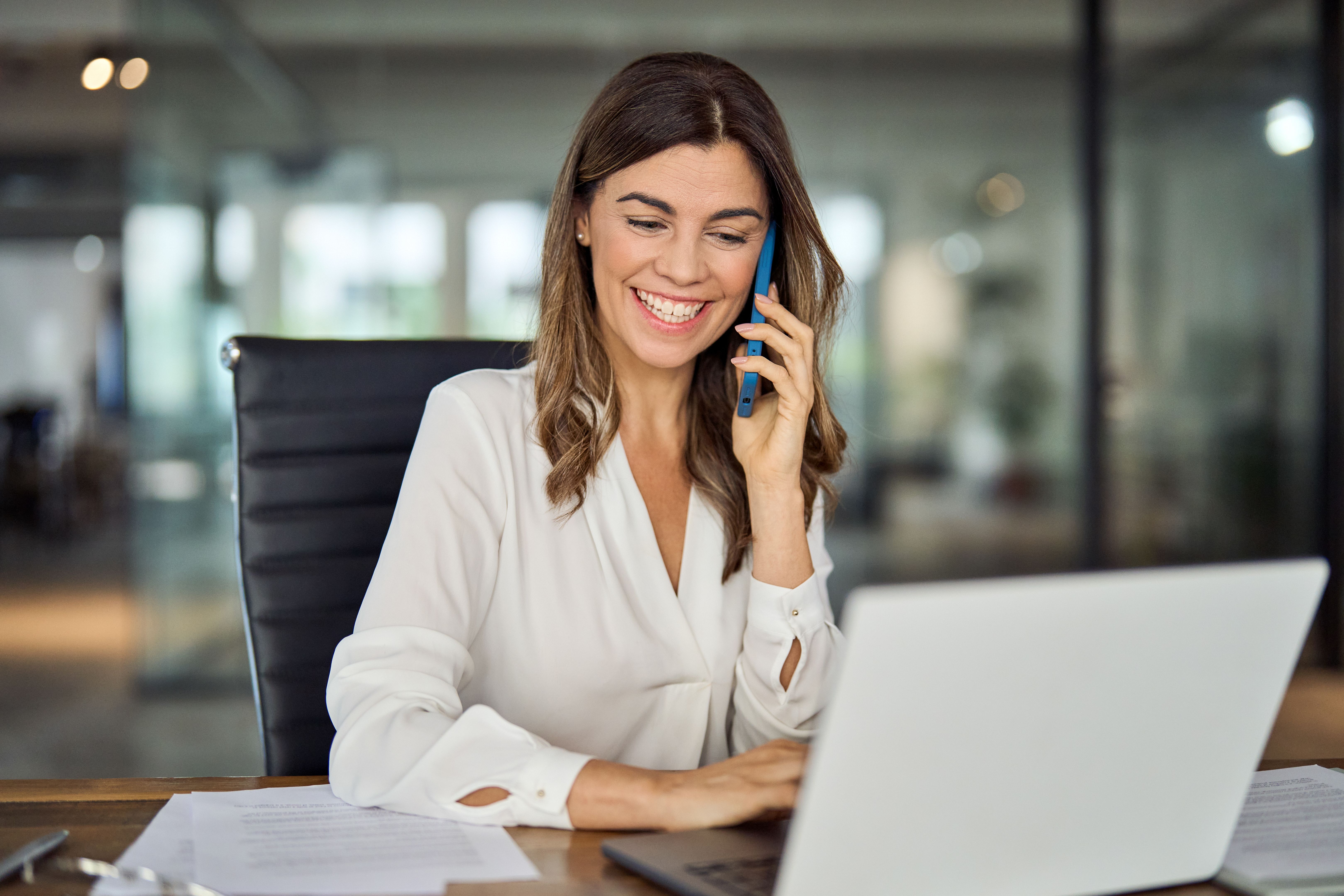 Happy mature business woman talking on phone making business call in office. Happy mature business woman talking on phone making business call in office.