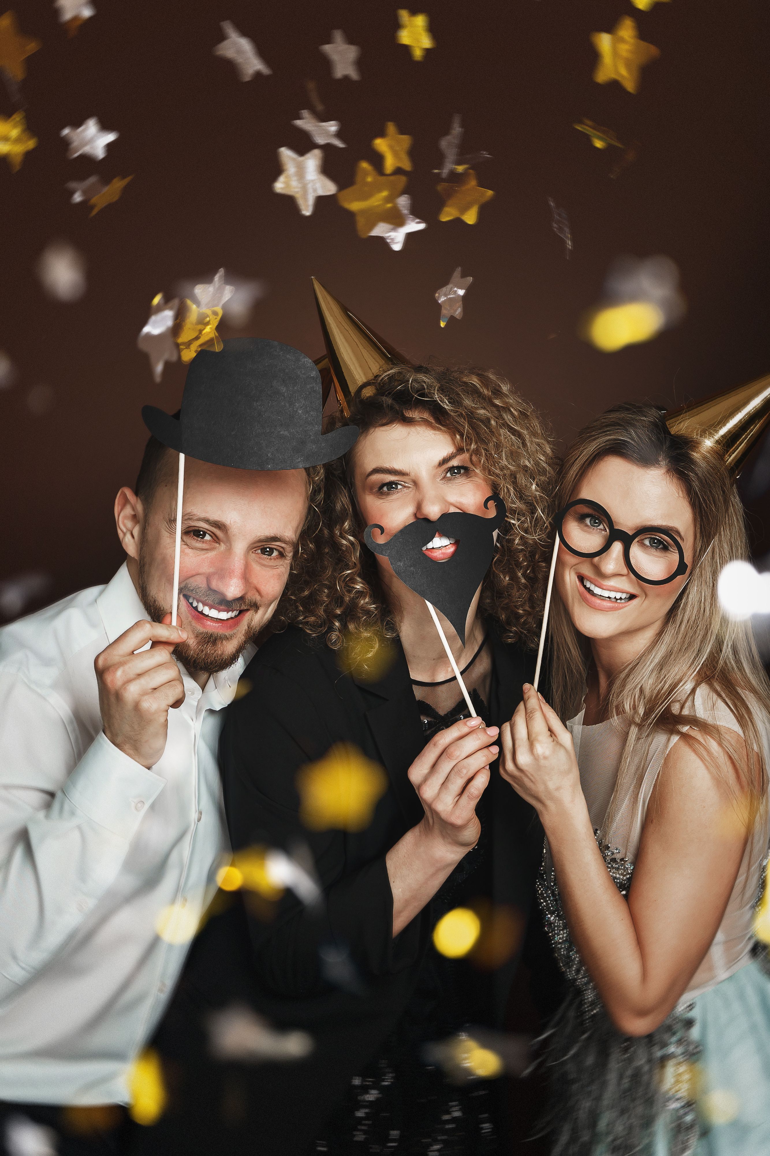 Group of happy people wearing party hats and using funny photo booth props are celebrating a holiday or event