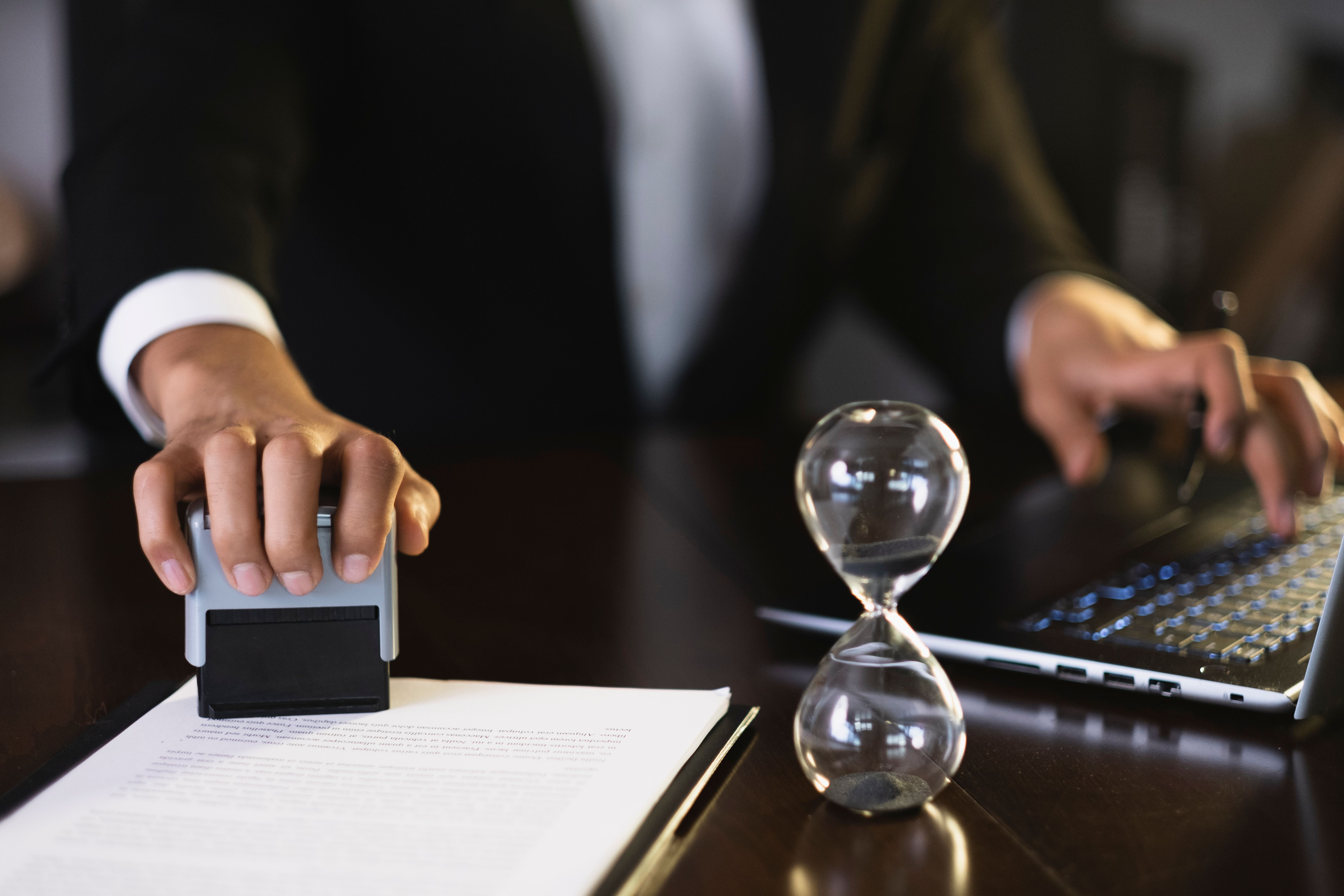 Businessman stamping document at desk with laptop and hourglass
