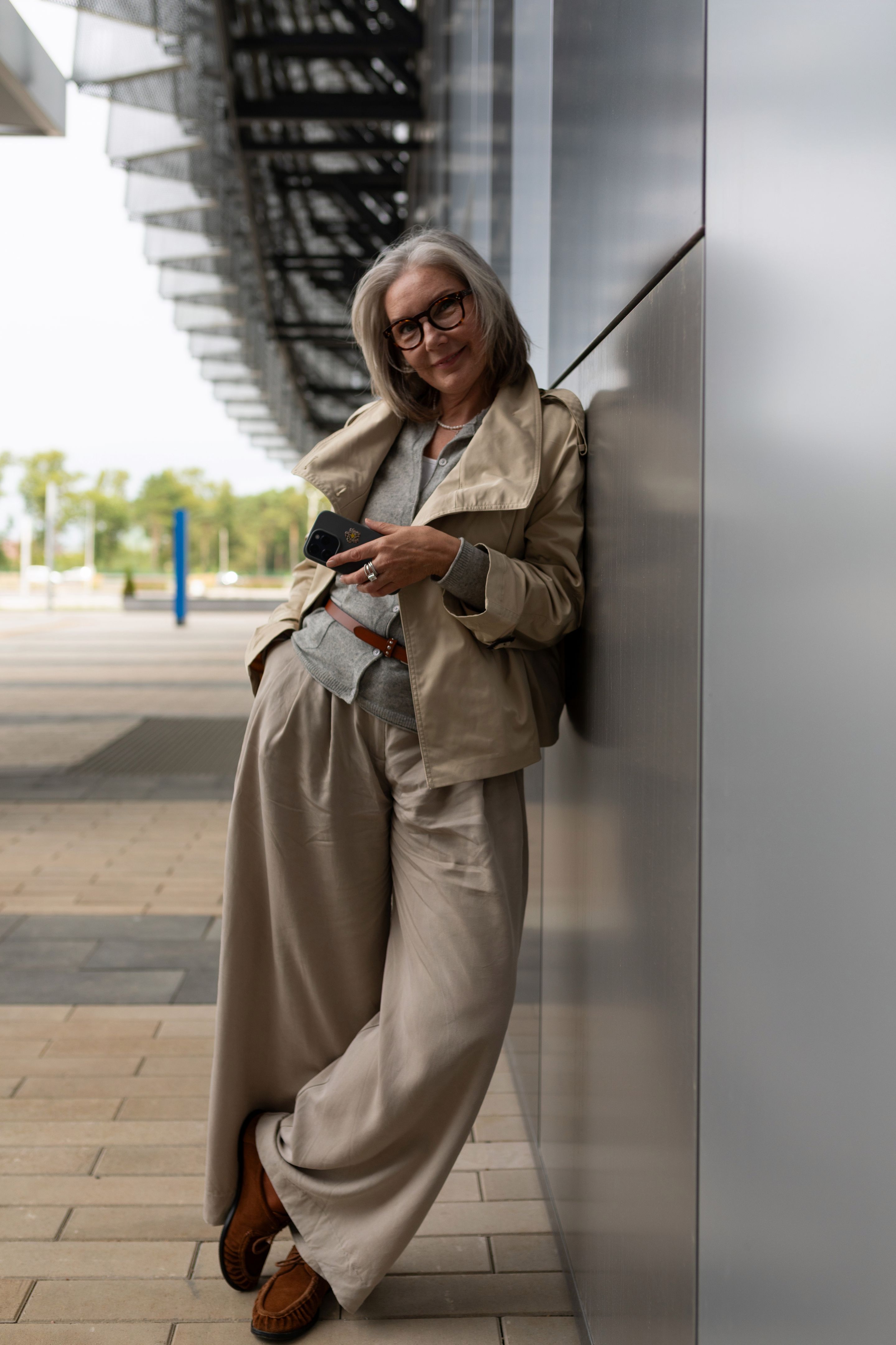 Elegant older woman relaxed and smiling while using smartphone near modern building in bright daylight