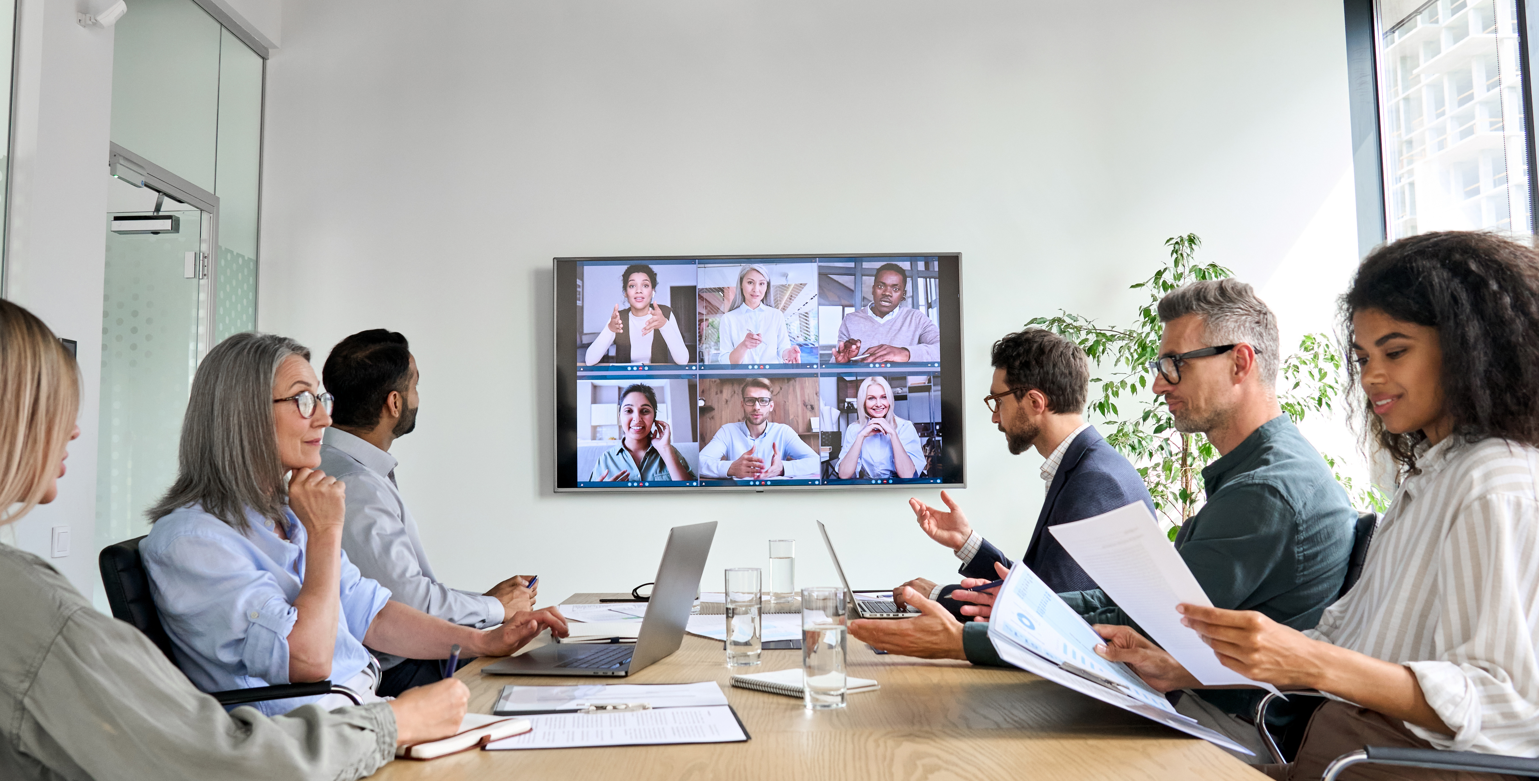 Diverse employees on online conference video call on tv screen in meeting room. Diverse employees on online conference video call on tv screen in meeting room.