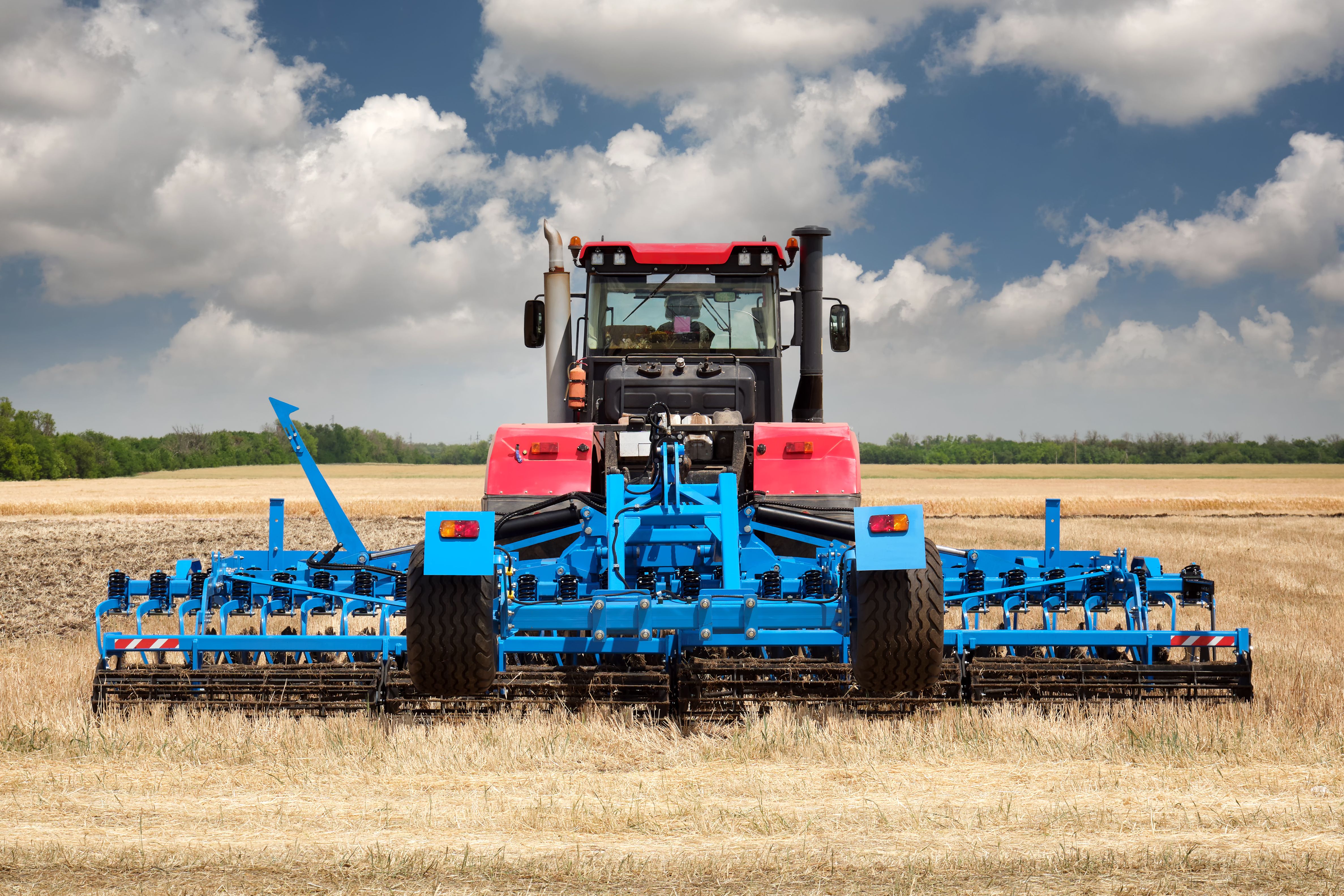 Rear view of a large tractor with a plow standing in a field.