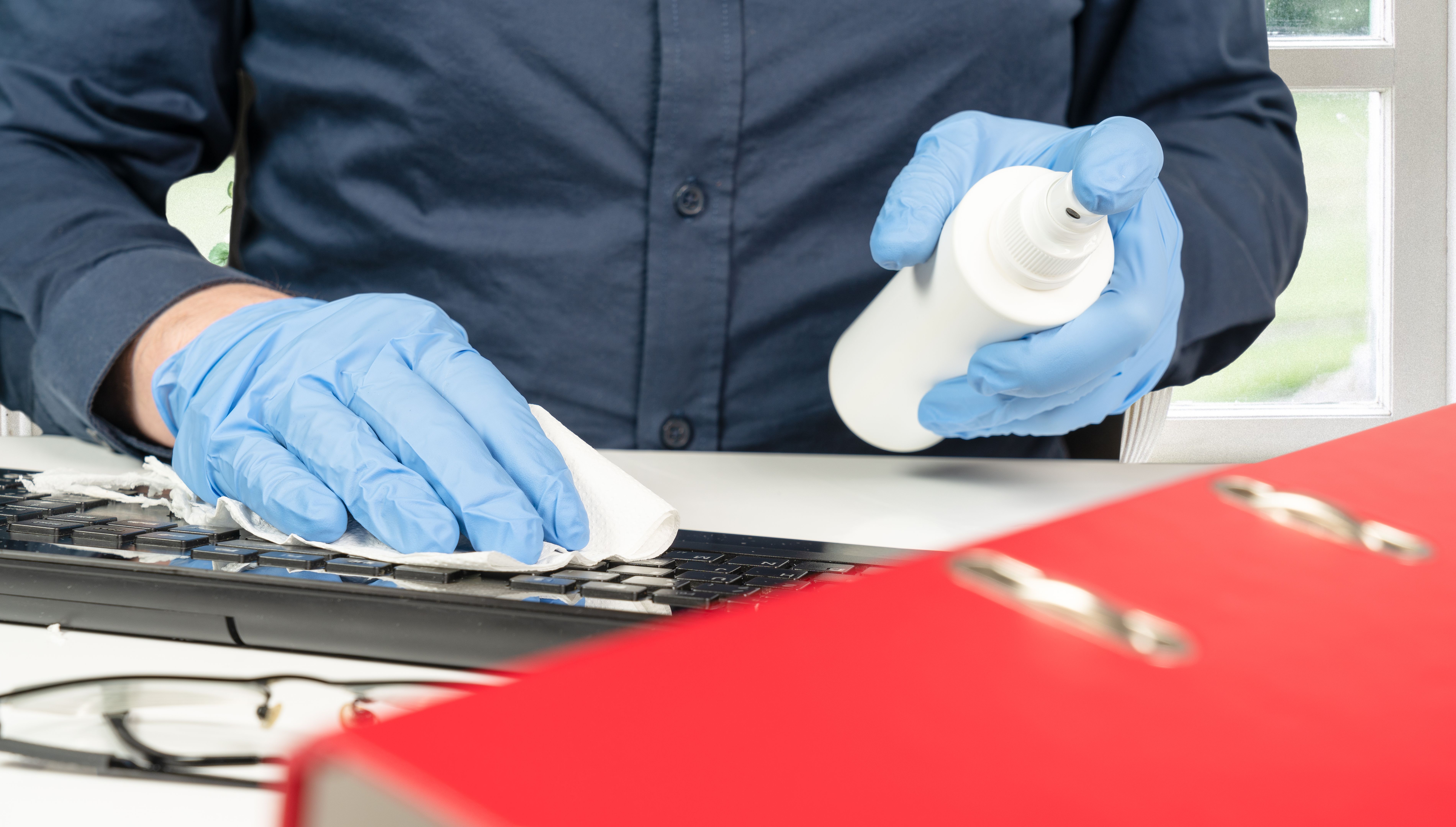 person cleans the office keyboard with a disinfectant