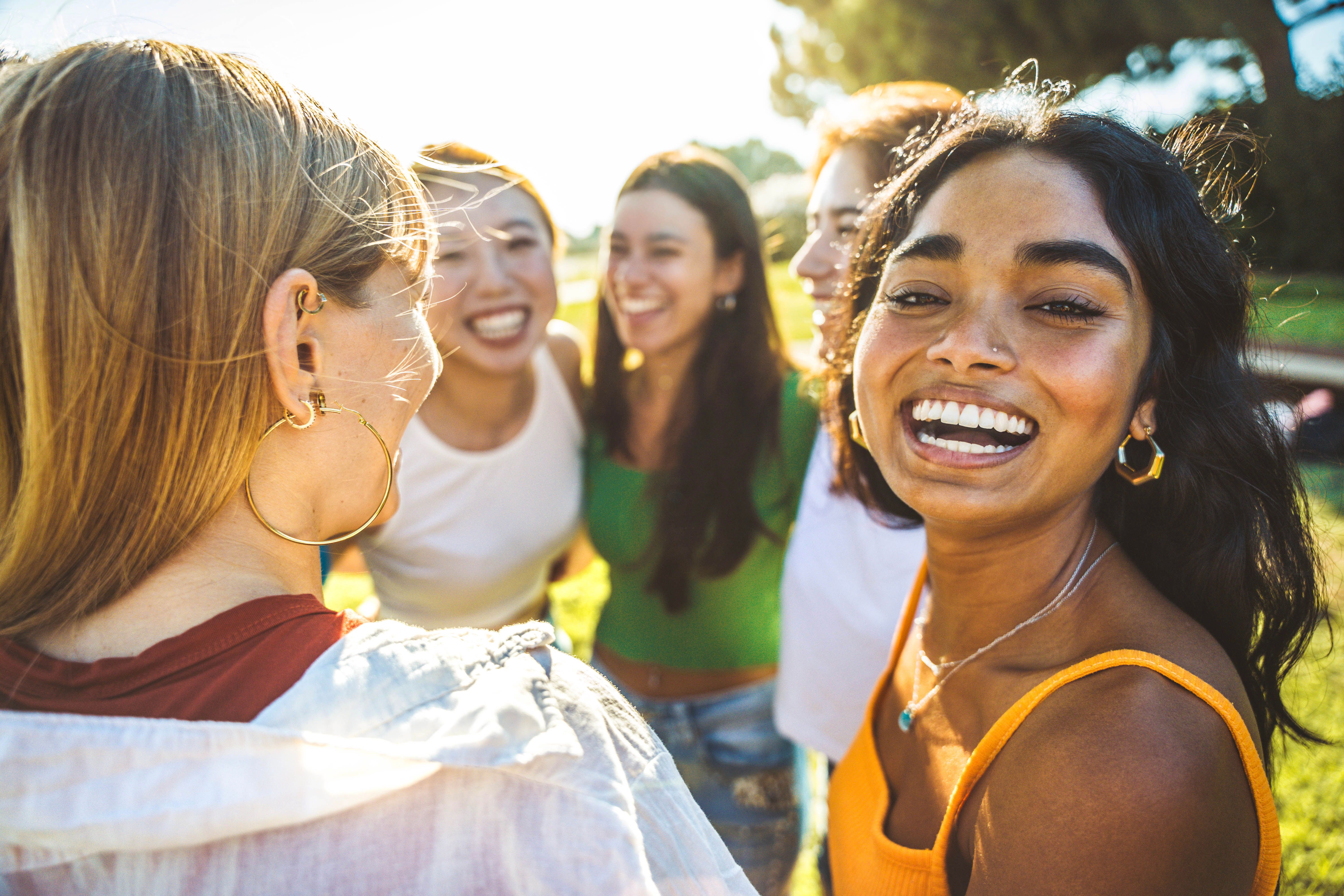 Happy group of young women hugging together outside - Cheerful black girl smiling at camera outdoors - Friendship and female community concept with multicultural girls having fun hanging out together
