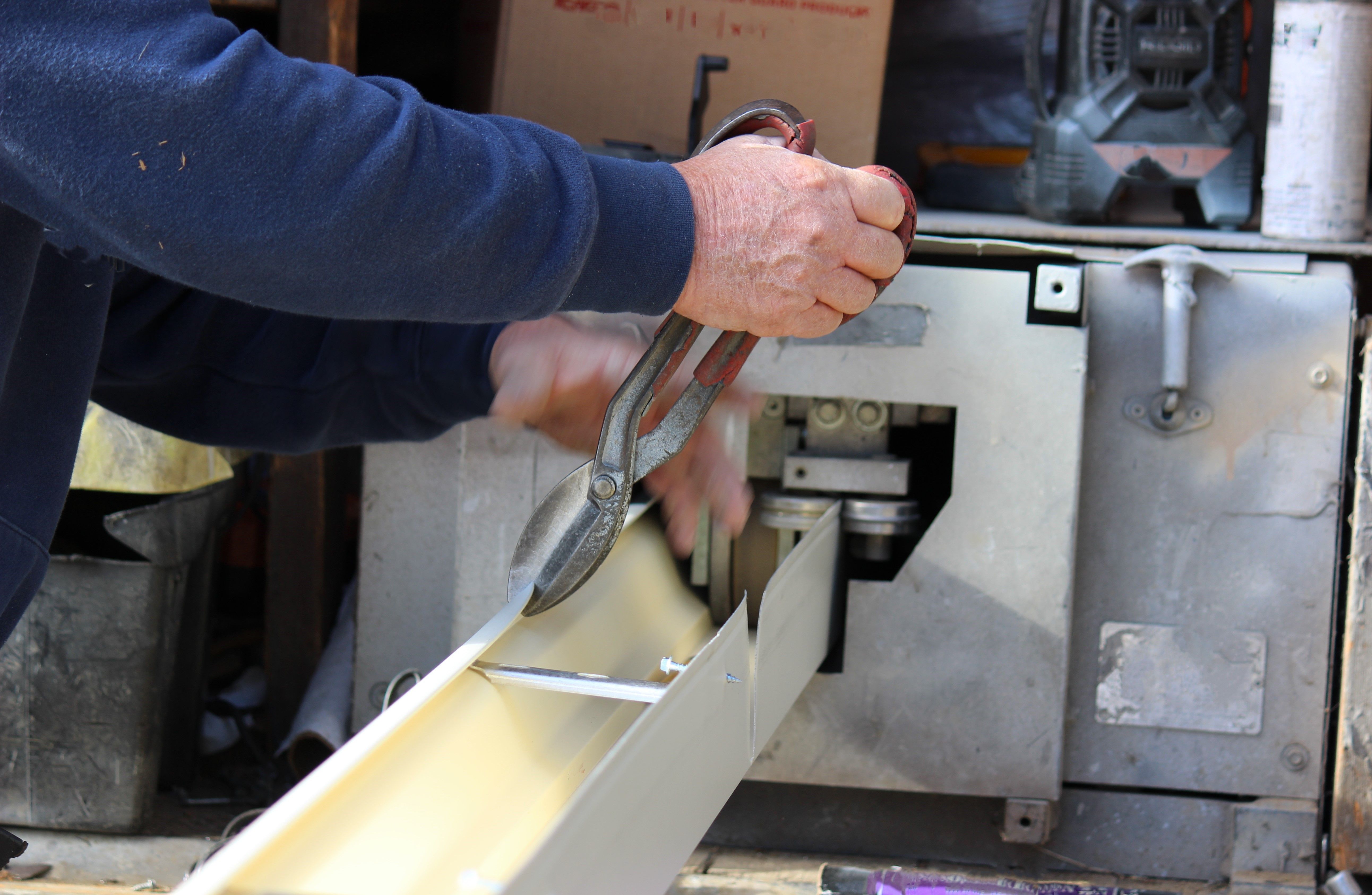 Roofing contractor preparing seamless gutter using a Seamless Gutter Machine to be installed on a residential building