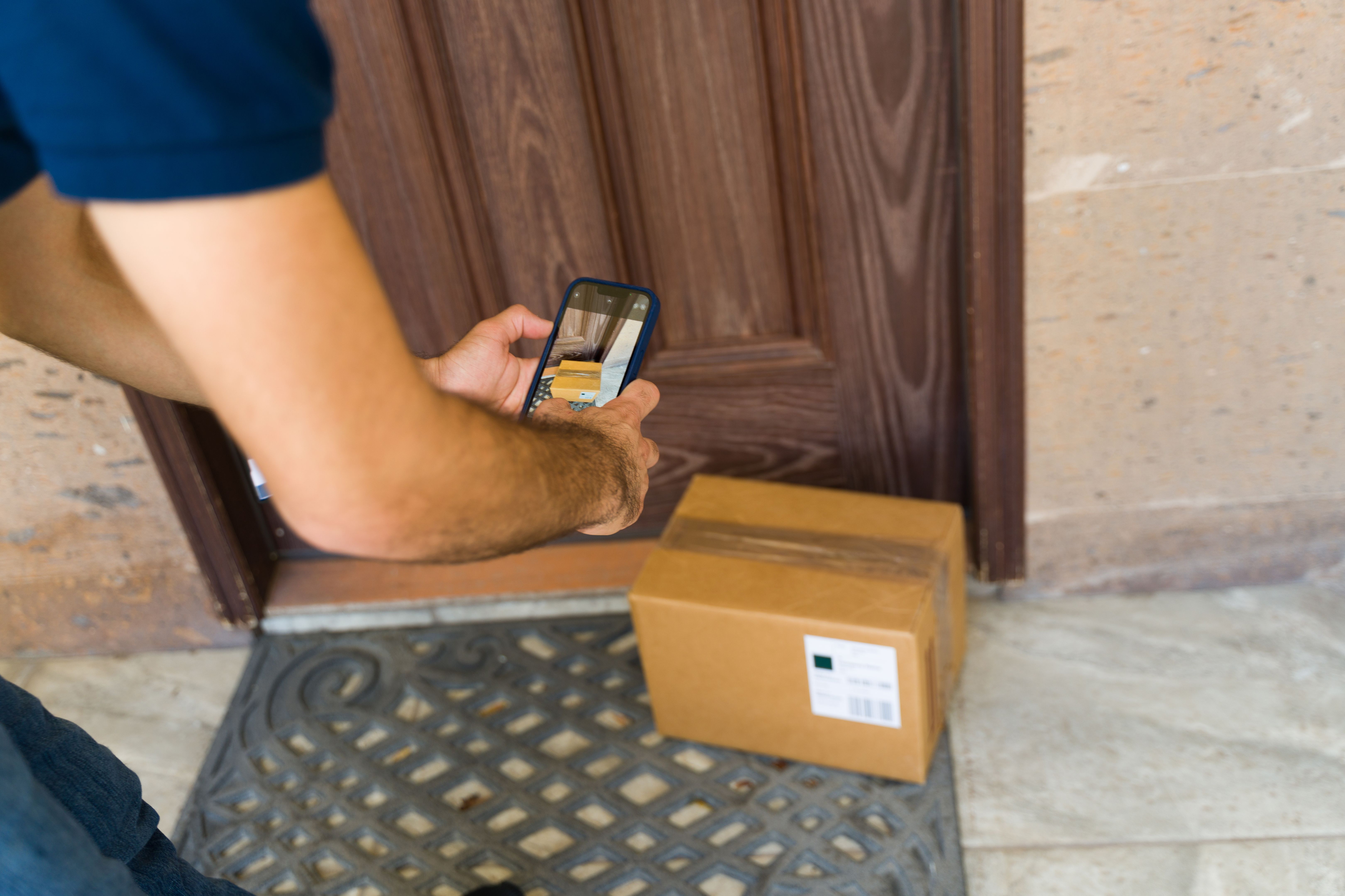 Delivery man capturing a photo of a freshly delivered package using his smartphone