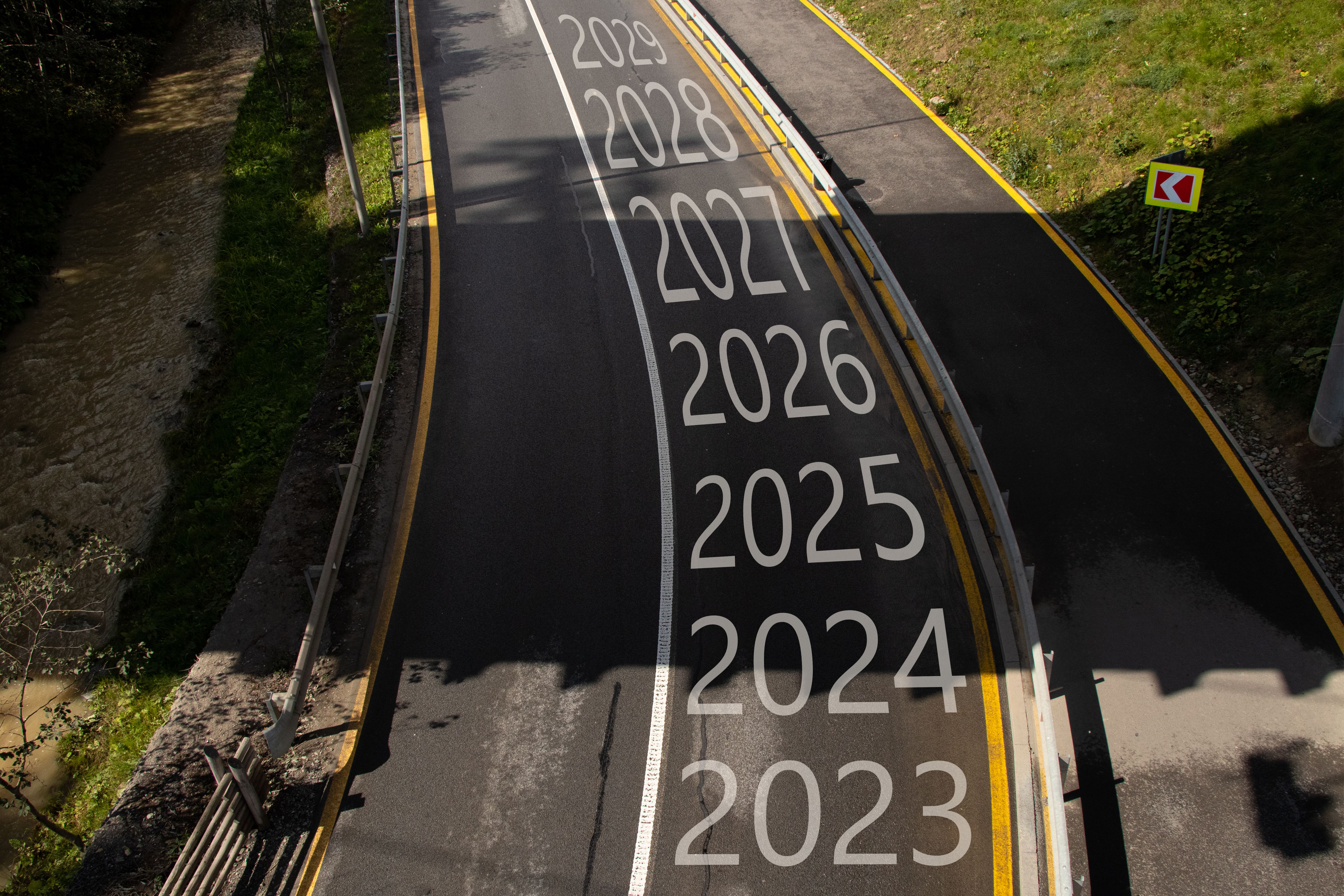 The years from 2023 to 2029 are written on the road with a turn to the left, the road goes in the mountains in the Carpathians and along the road there is a mountain river, Bukavel The years from 2023 to 2029 are written on the road with a turn to the left, the road goes in the mountains in the Carpathians and along the road there is a mountain river, Bukavel